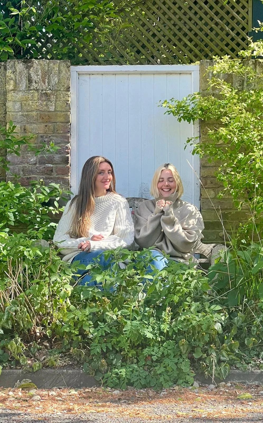 Two women sitting on a bench smiling surrounded by plants