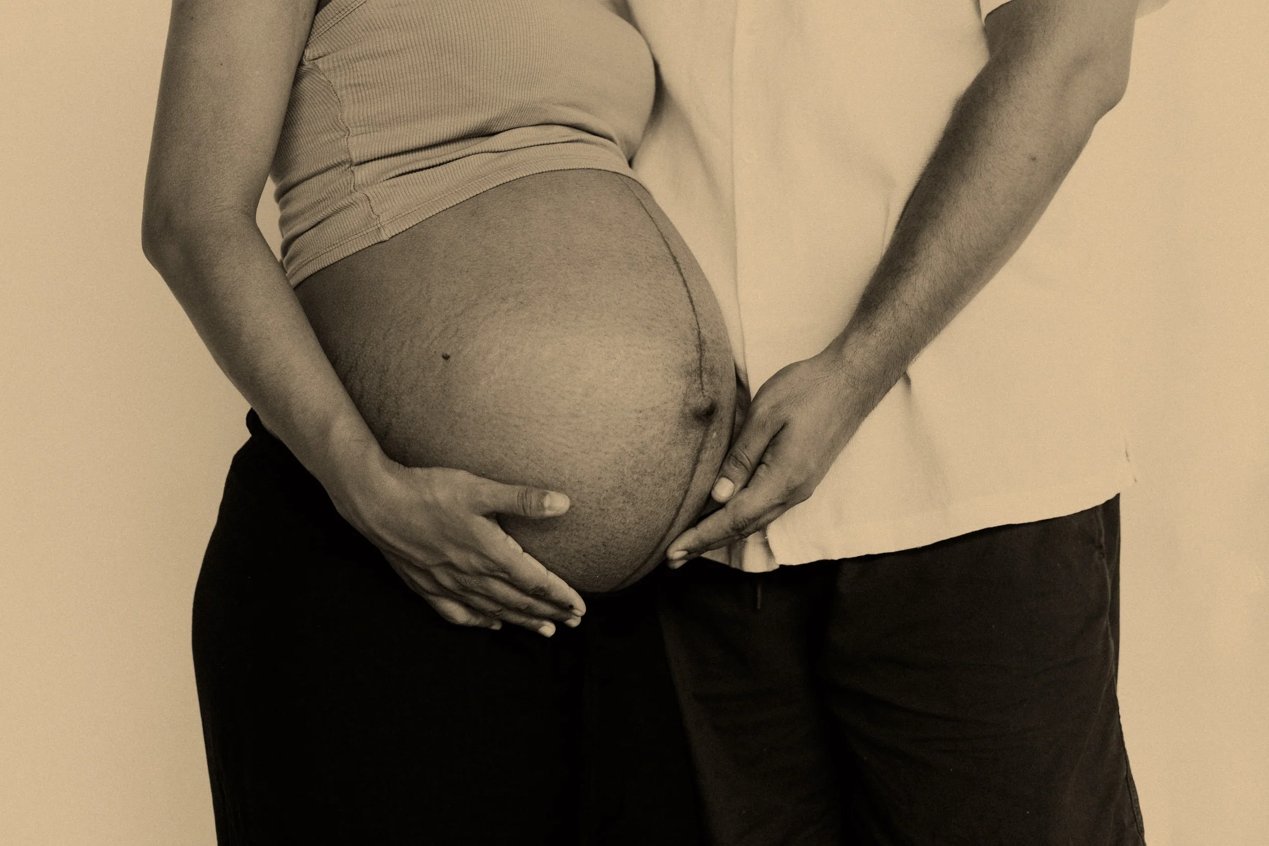 A pregnant woman with a man holding her belly with both hands.