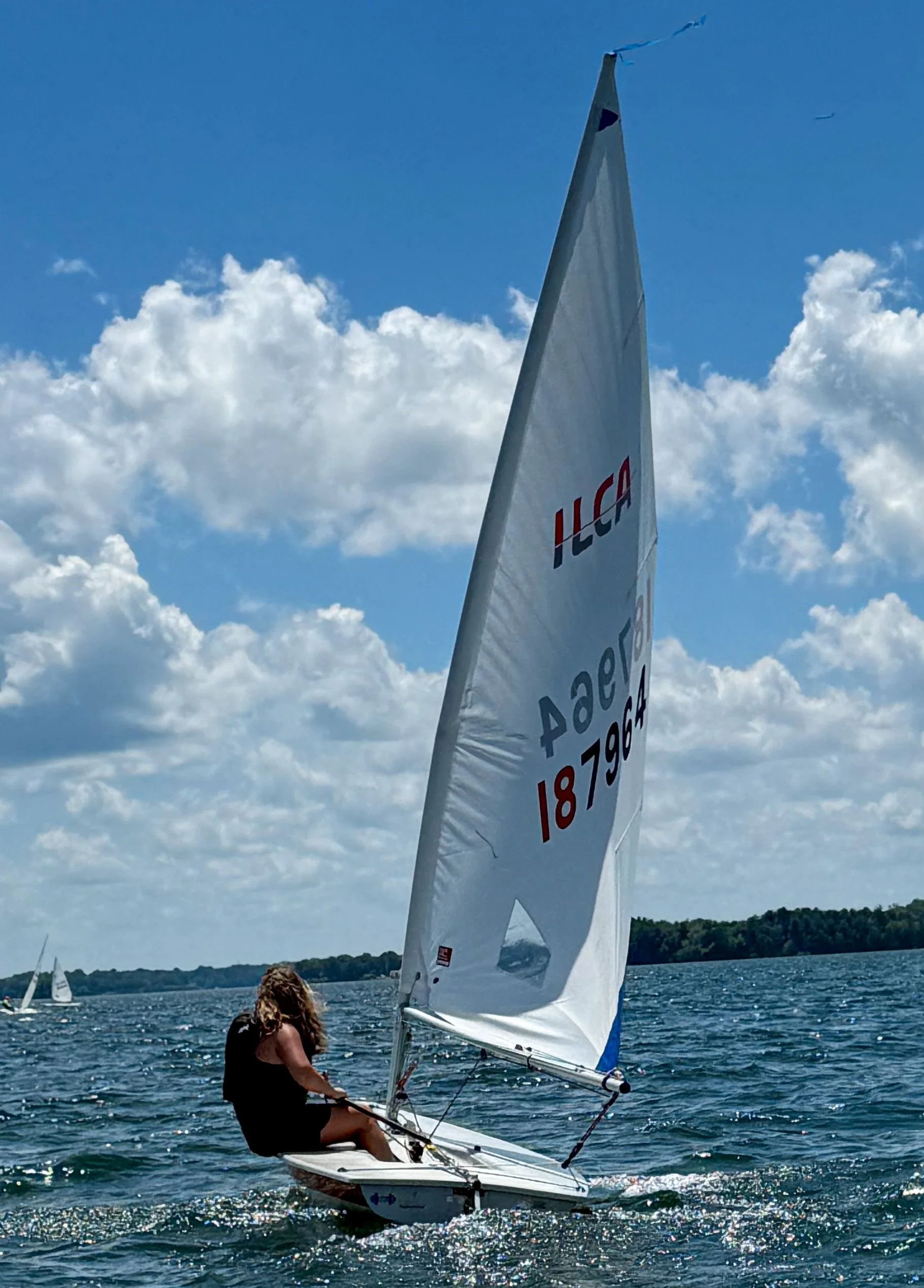 A woman sailing a small sailboat on a lake with a partly cloudy sky in the background -  - Mainecoon Gods LLC