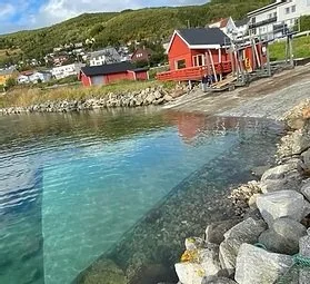 Klart vann ved en kystby med fargerike hus og fjell i bakgrunnen.