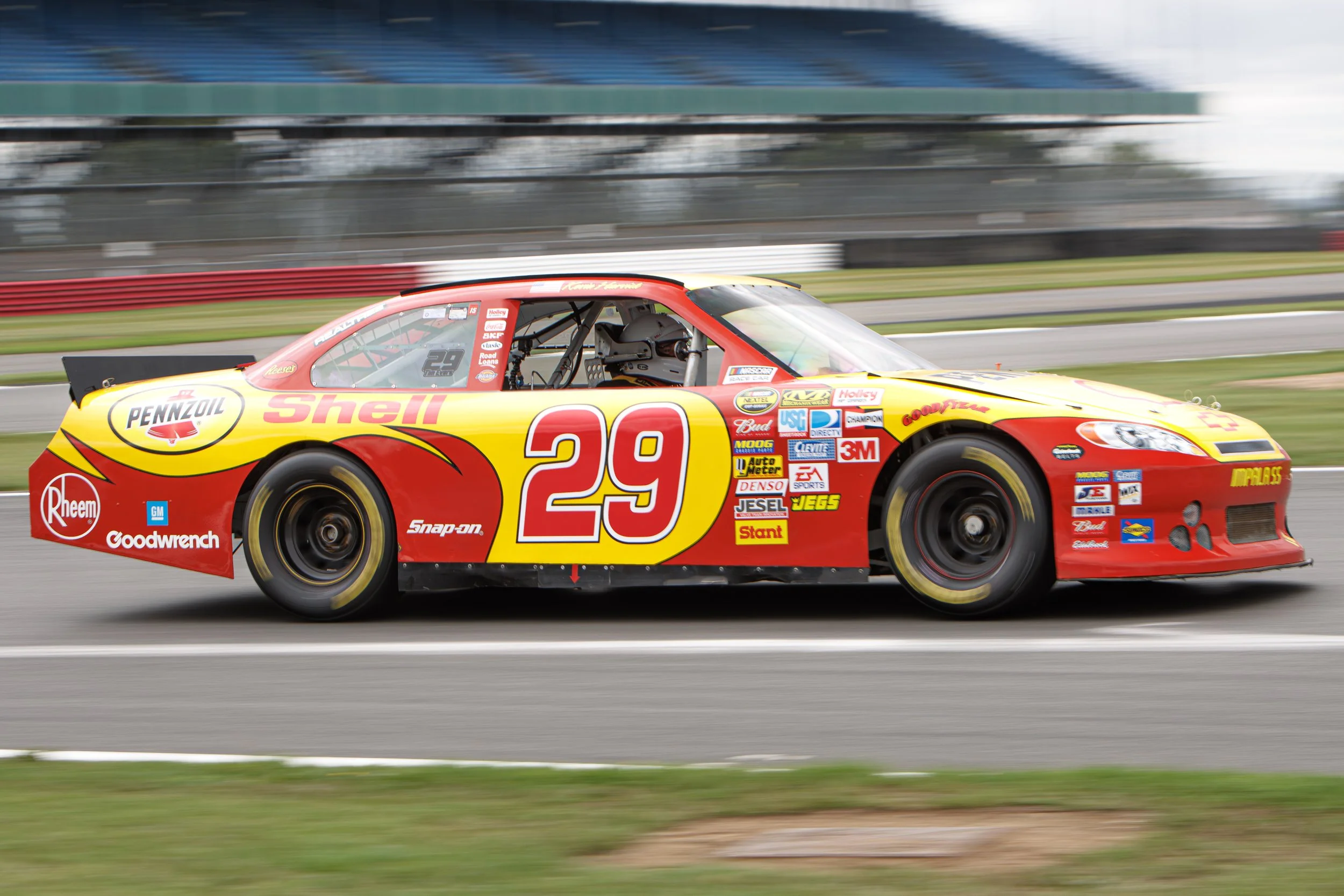 Race car with red and yellow paint, bearing the number 29 and large sponsor logos, moving on a race track.
