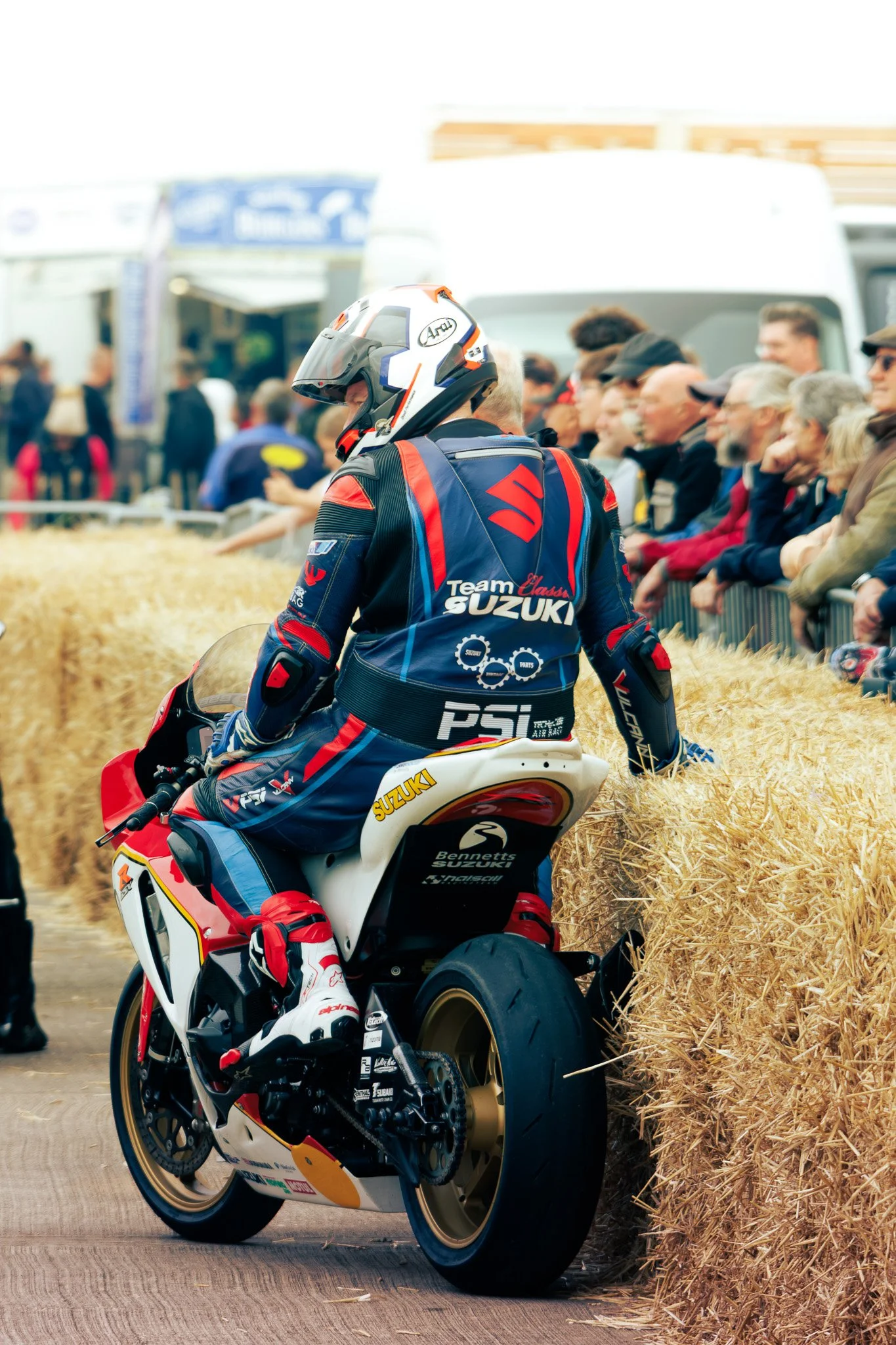 A motorcycle racer in racing gear sitting on a Suzuki motorcycle, with a crowd of spectators watching at a racing event.