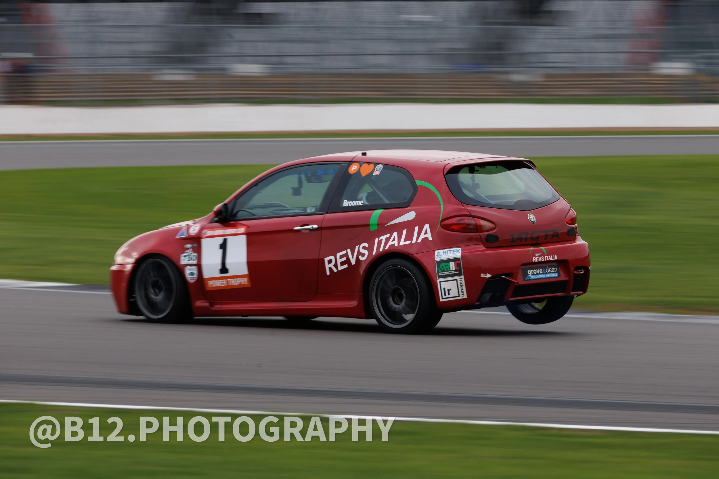 Red race car with 'REVS ITALIA' and the number 1 on the side, driving on a race track during daytime.