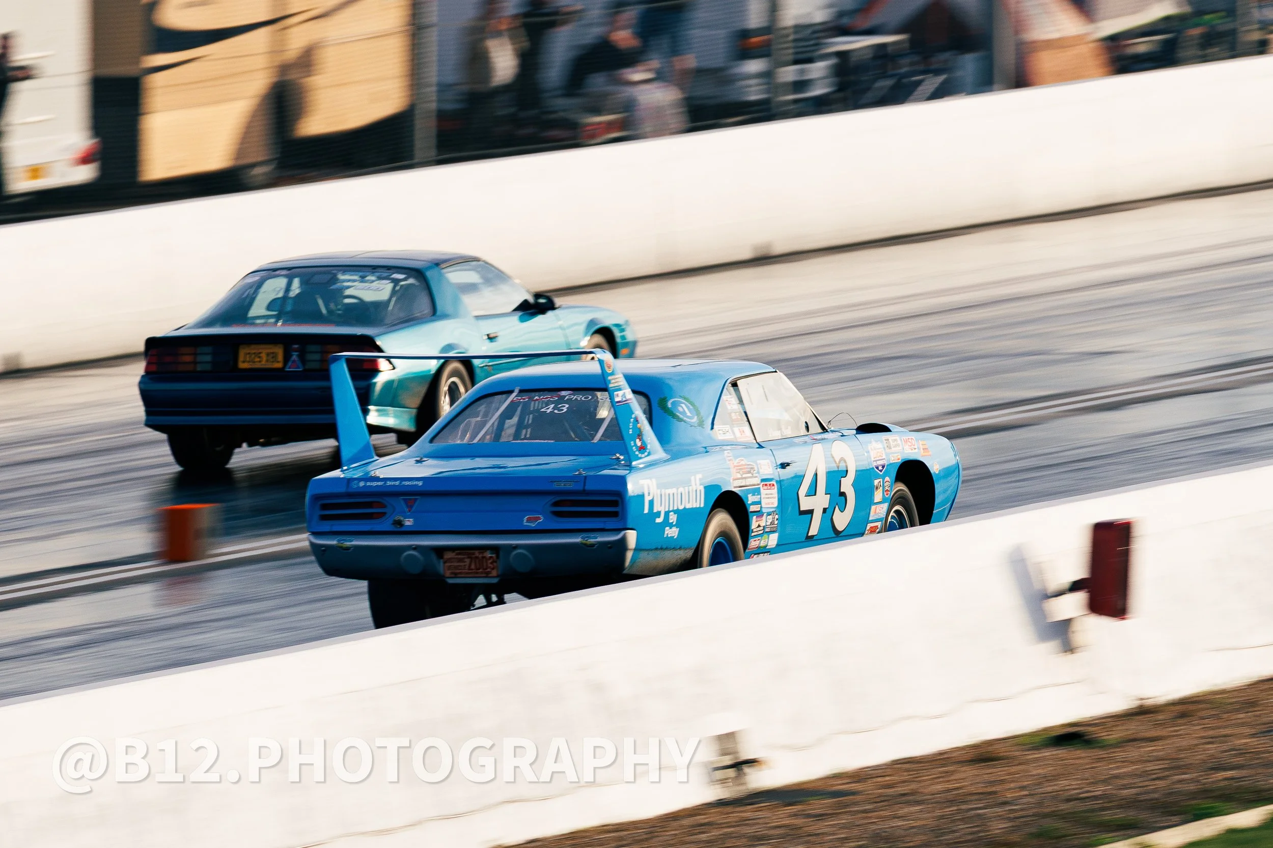 Two race cars, one with the number 43 and another with the number 44, racing on a track with spectators in the background.