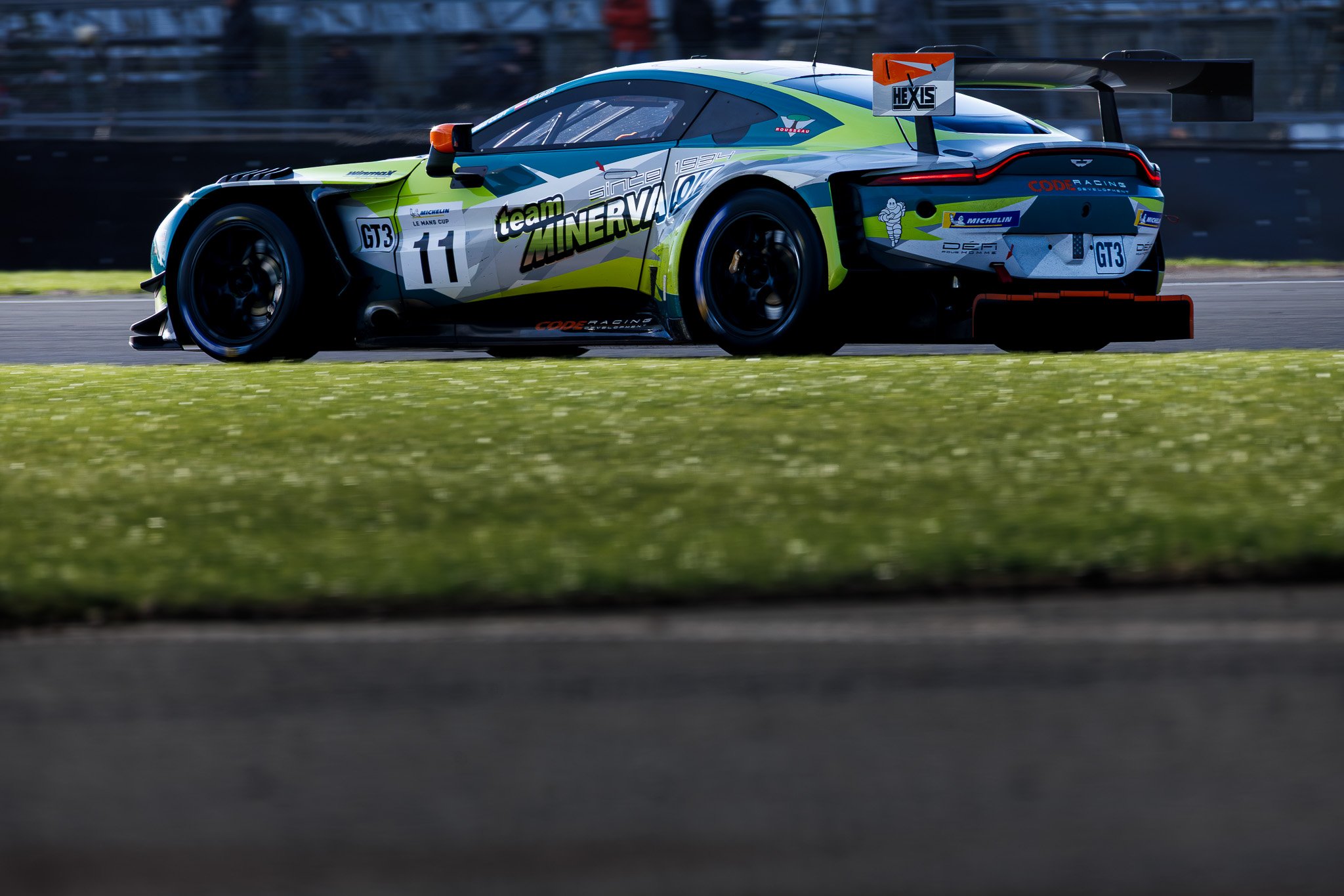 A race car on a track with a bright green and gray color scheme, labeled with the number 11 and logos including Team Minerva and Michelin.