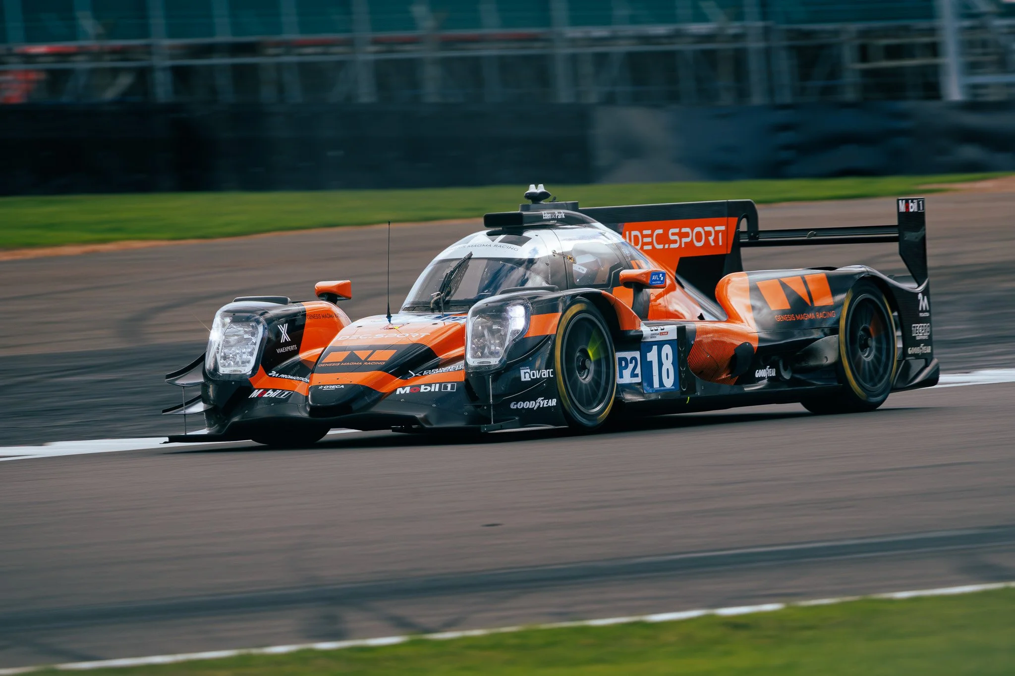 A sleek, black and orange open-wheel race car speeding on a racetrack with a blurred background.