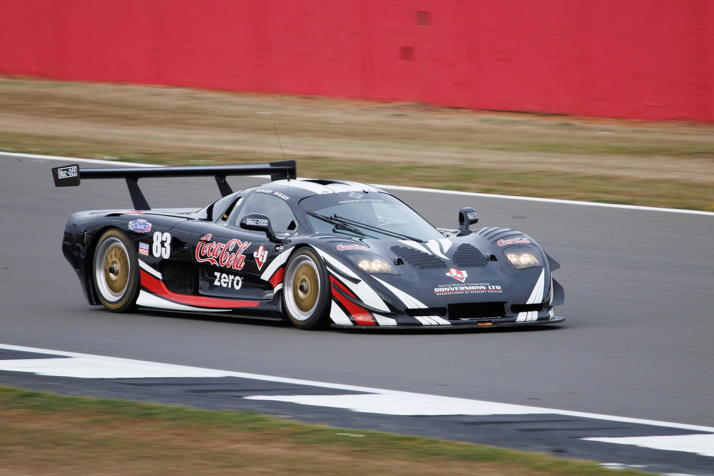 A black and white racing car with sponsor logos, including Coca-Cola Zero, speeding on a race track with a blurred background.