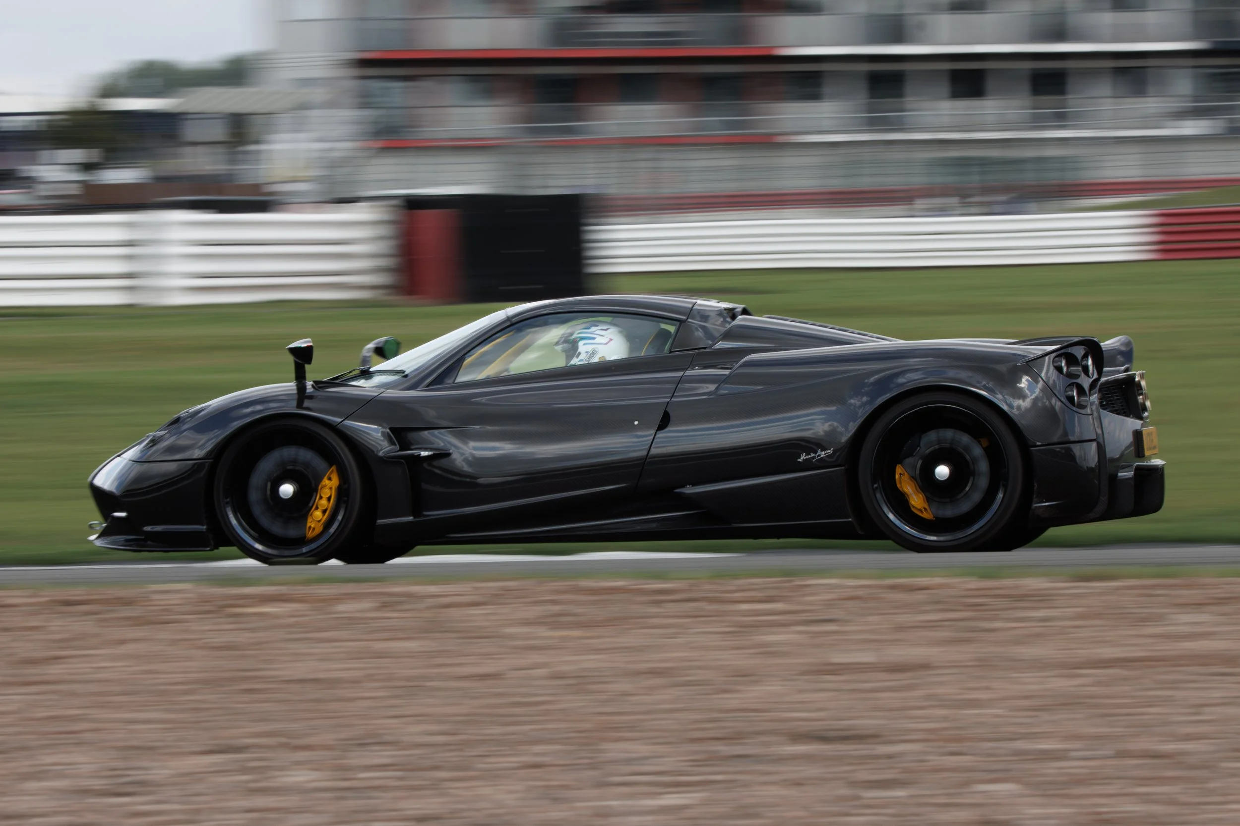 Black race car on a race track in motion, with a driver inside wearing a helmet.