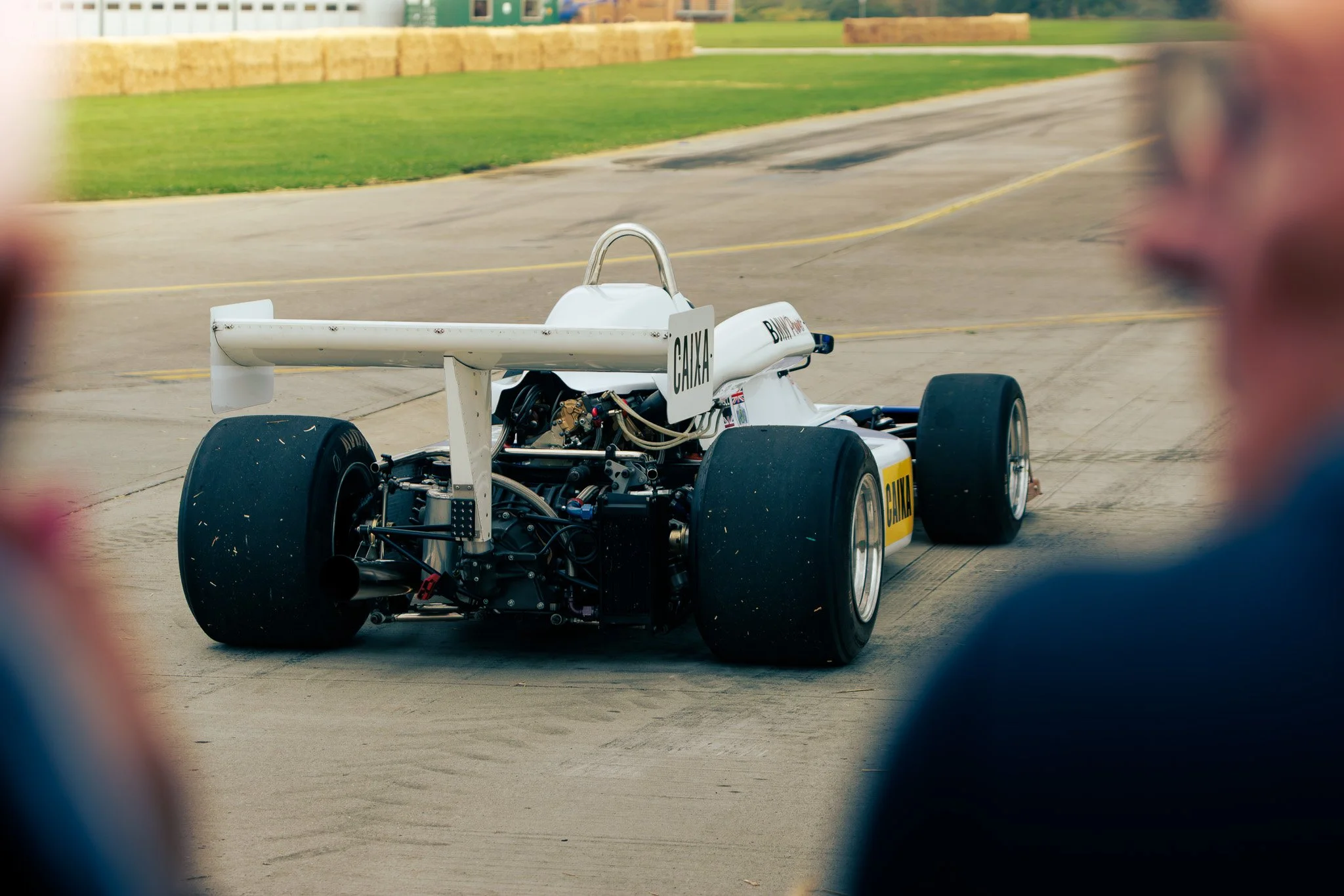 Race car on a concrete track, viewed from behind with blurred spectators in the foreground.