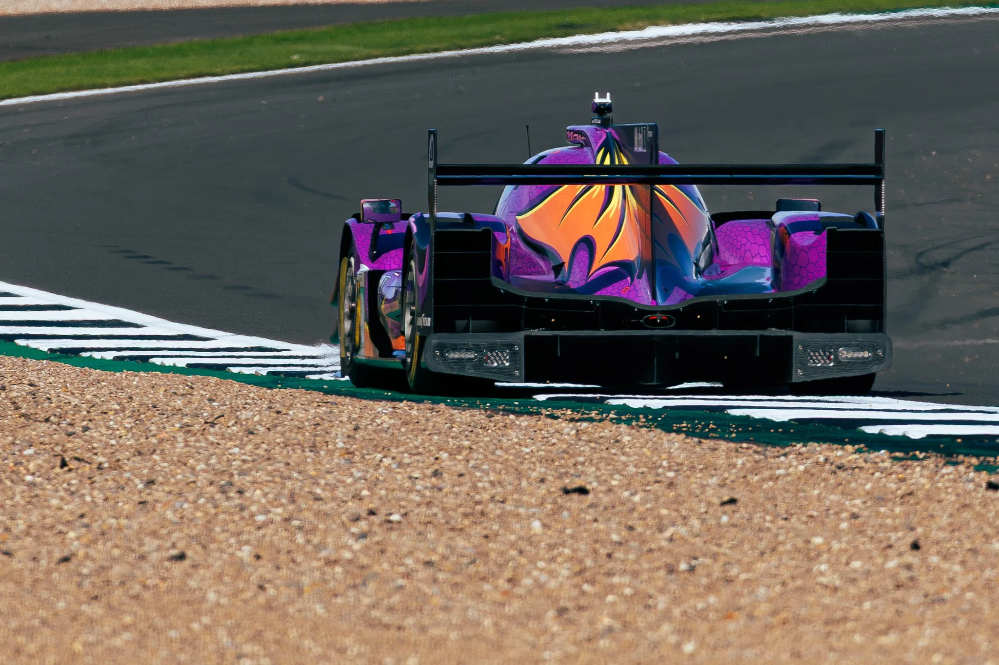 A colorful race car with a purple, orange, and yellow paint design on a race track.