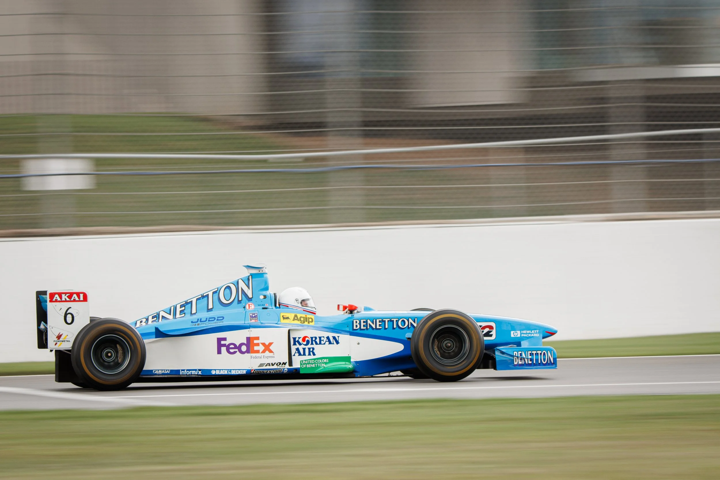 Race car on a track with sponsor logos including Benetton, FedEx, and Korean Air, moving at high speed with a blurred background.