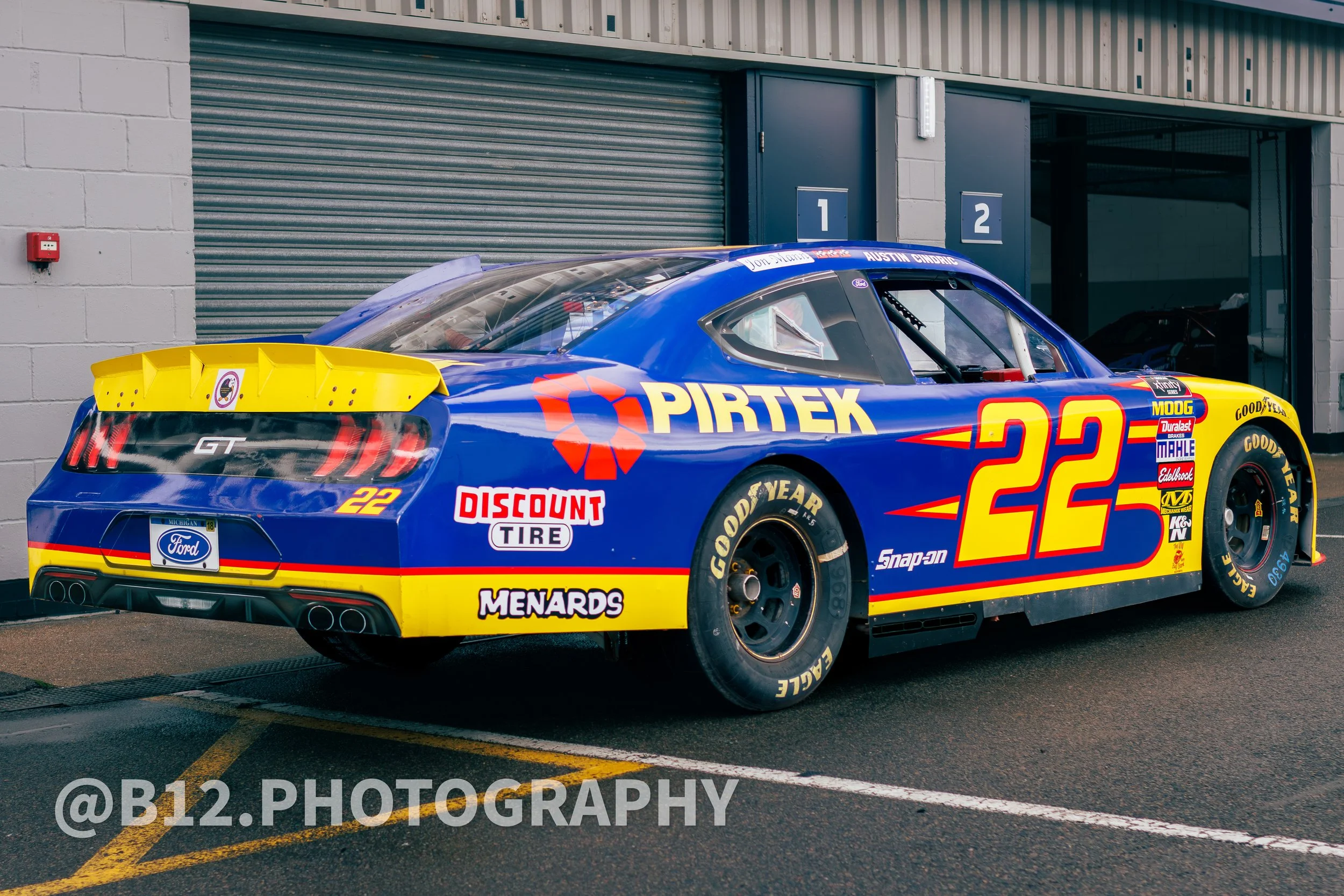 A blue and yellow race car with the number 22 on its side, parked inside a garage with a closed gray garage door in the background.