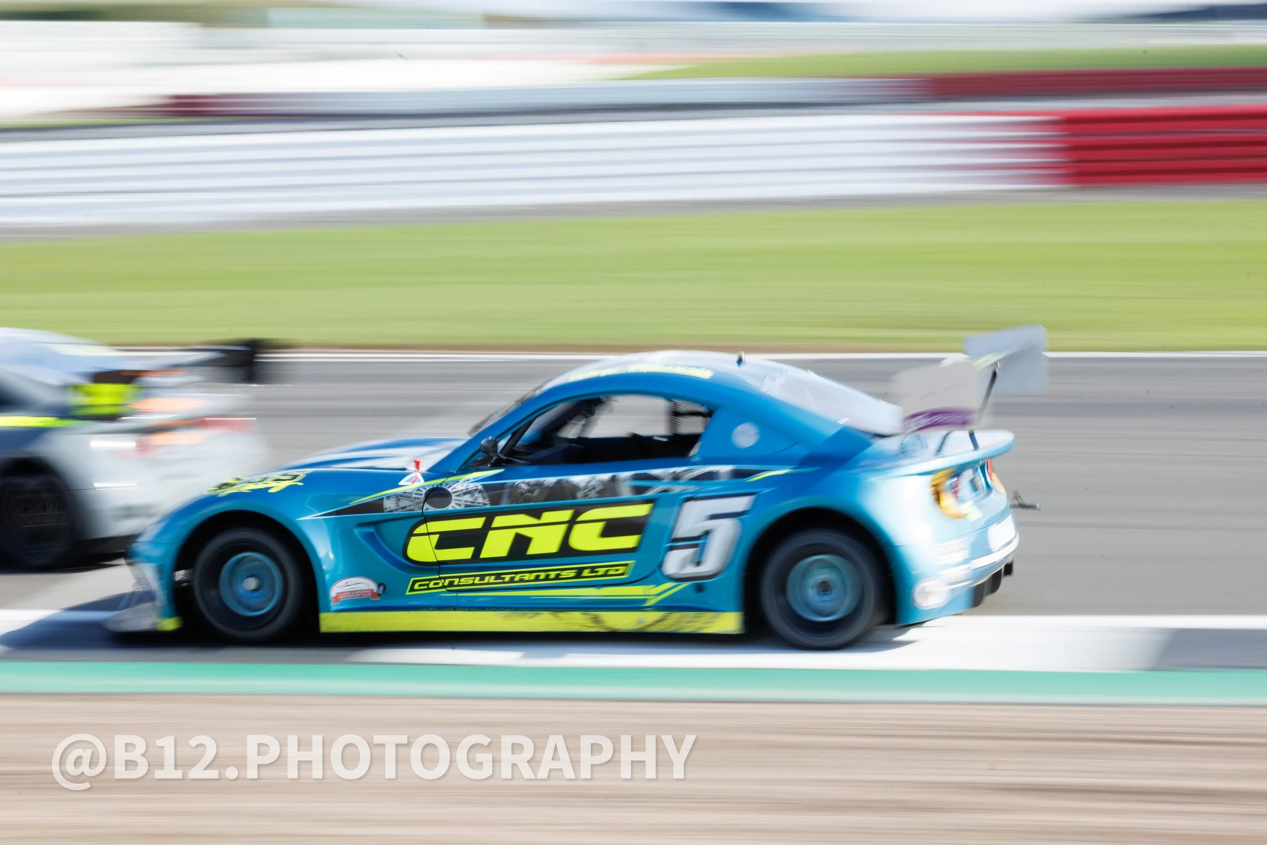 Blue race car with the number 5 speeding on a racetrack, with blurred background and other racing cars.