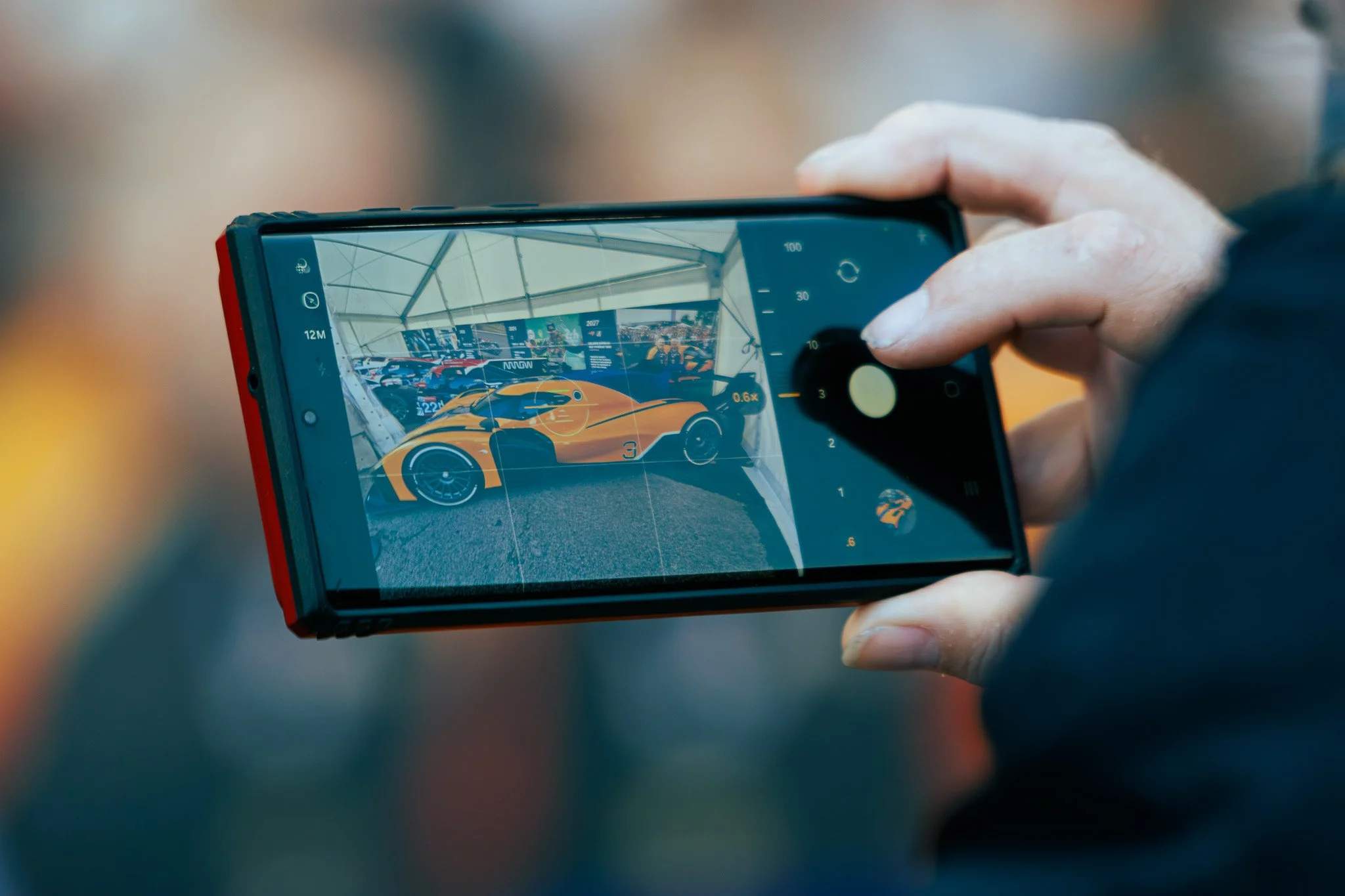 Person taking a photo of a yellow race car with a smartphone