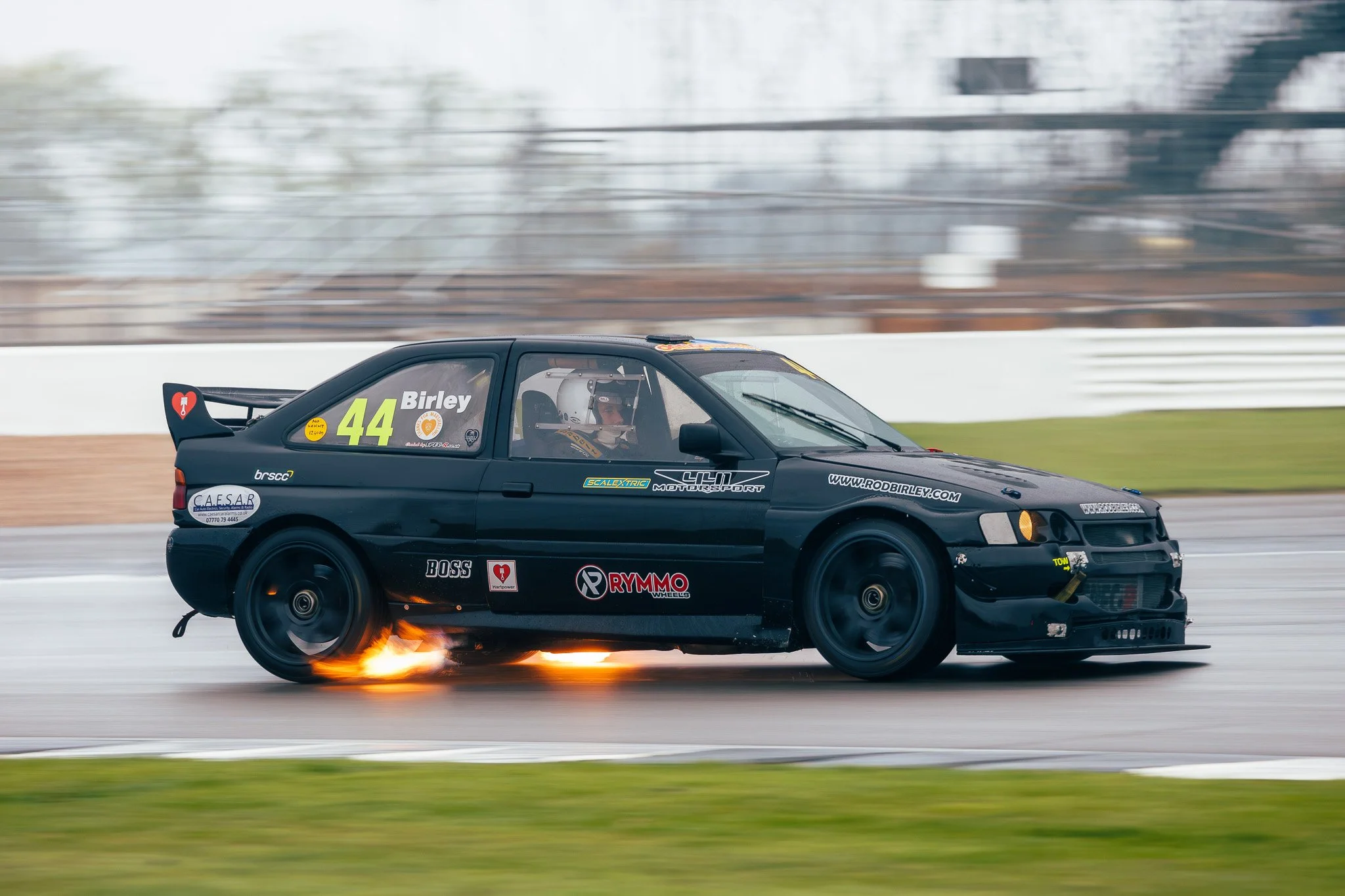 Black race car with flames coming from the exhaust driving on a race track.