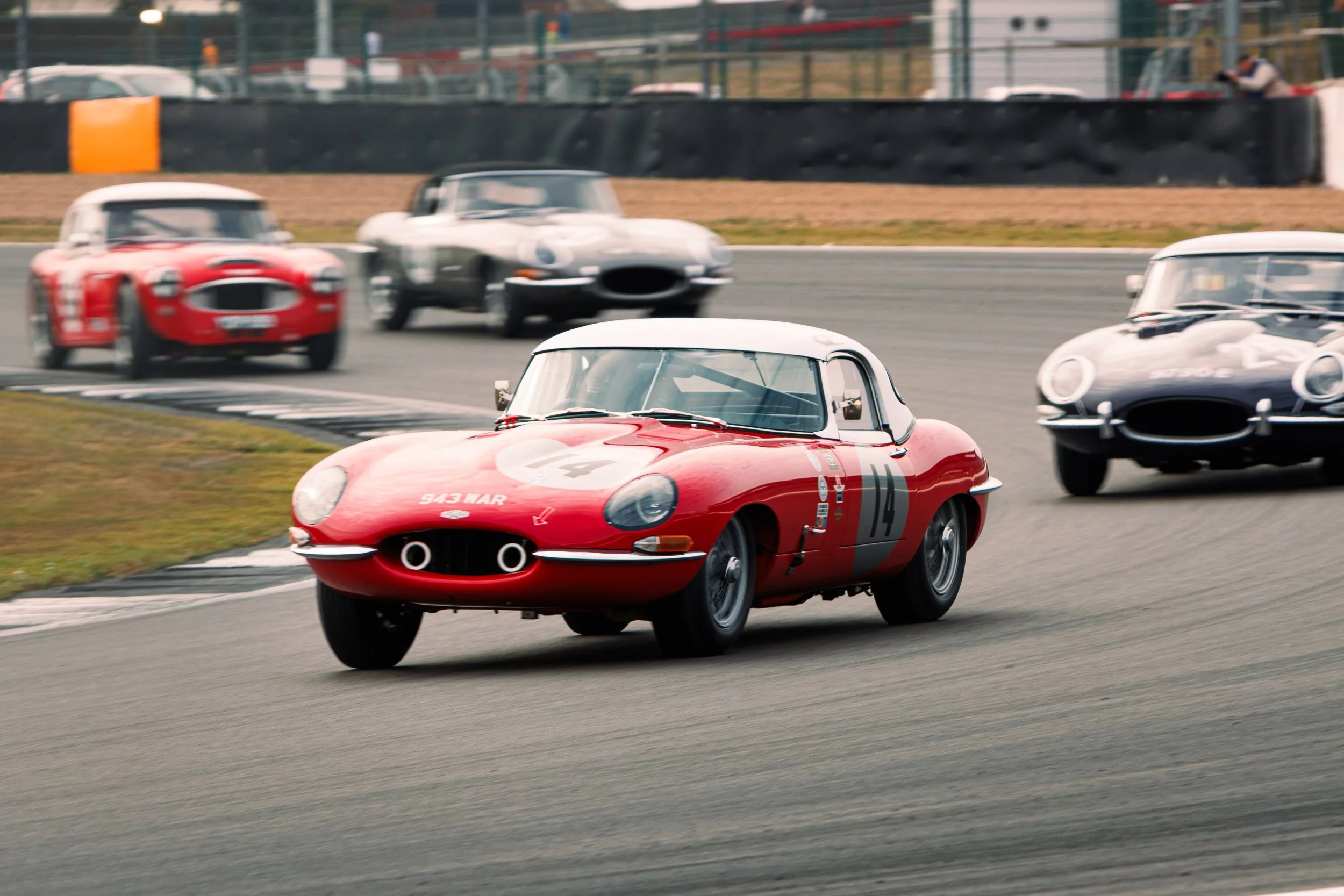 Vintage race cars, including a red and white sports car, racing on a track.