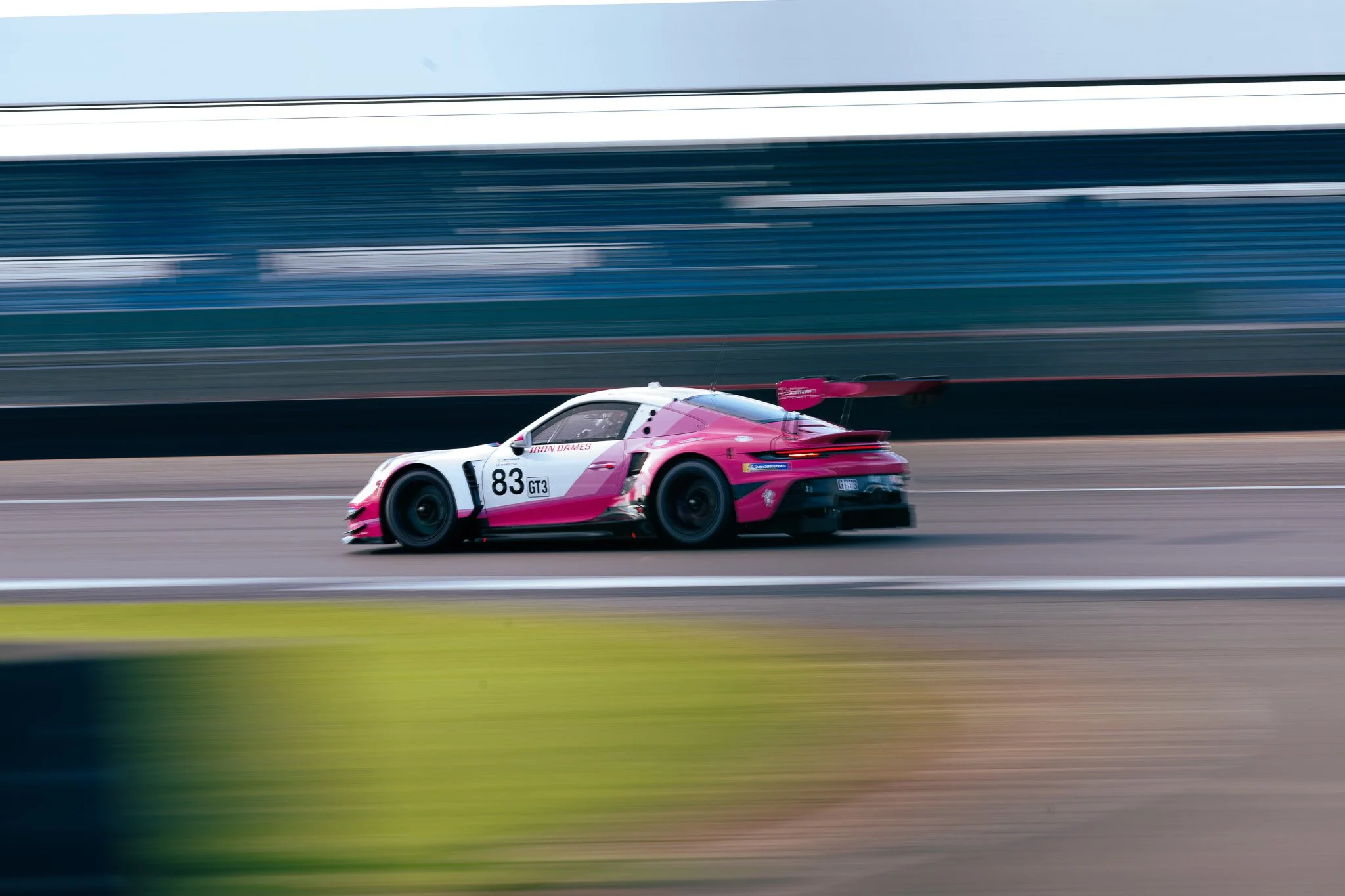 Pink and white race car speedily moving on a race track with a blurred background, number 83, labeled GT3.