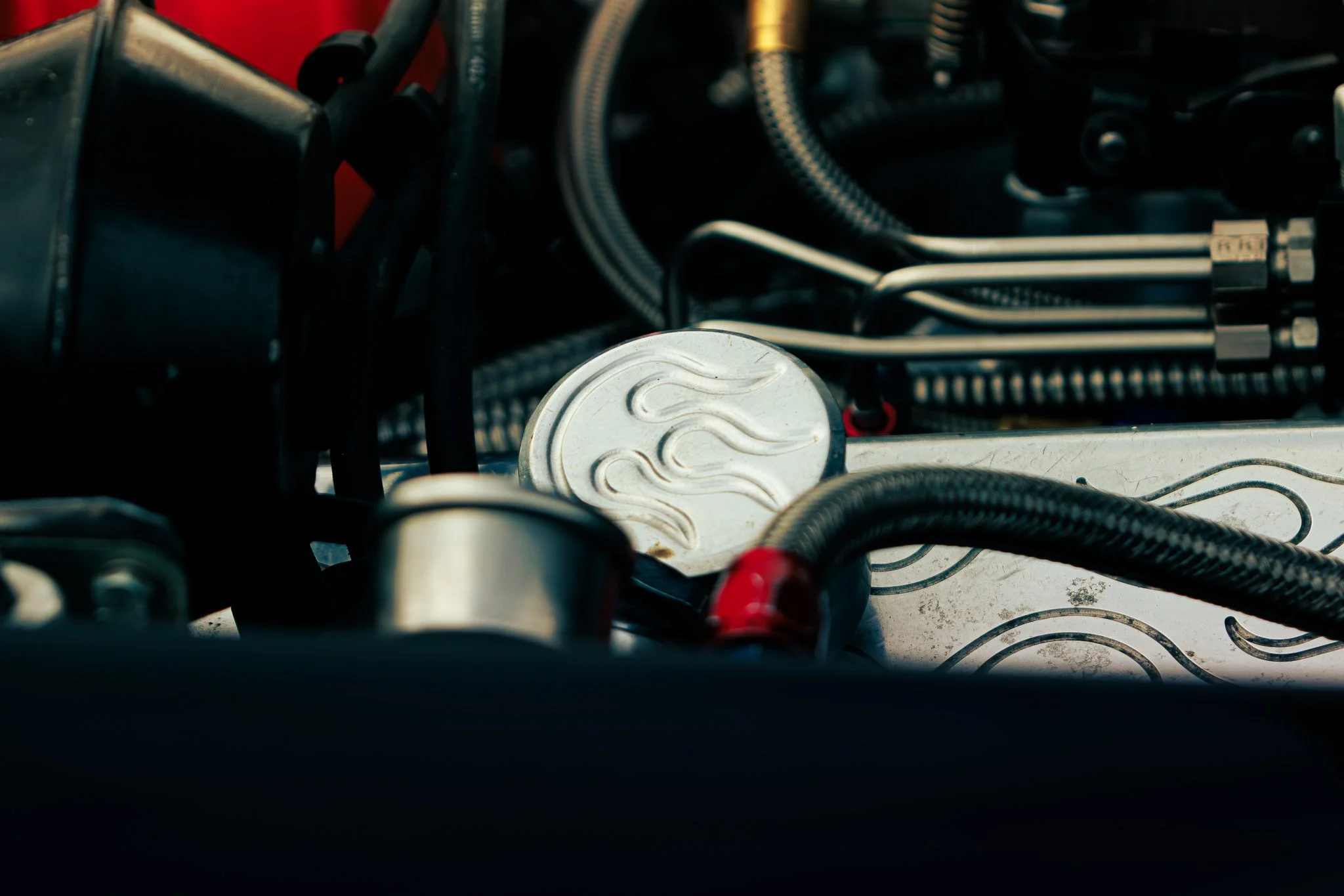 Close-up of a car engine with a metal plate featuring flame engraving, surrounded by various black hoses and metallic parts.