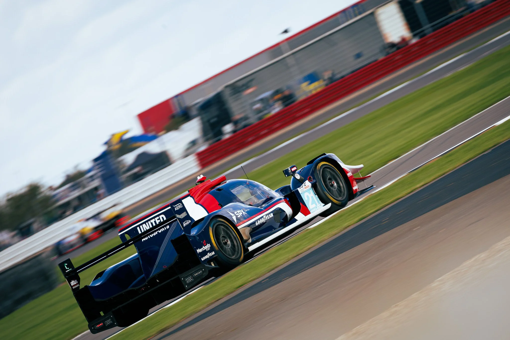 A race car with the number 21 on the side, painted in blue, white, and red, speeding on a race track.