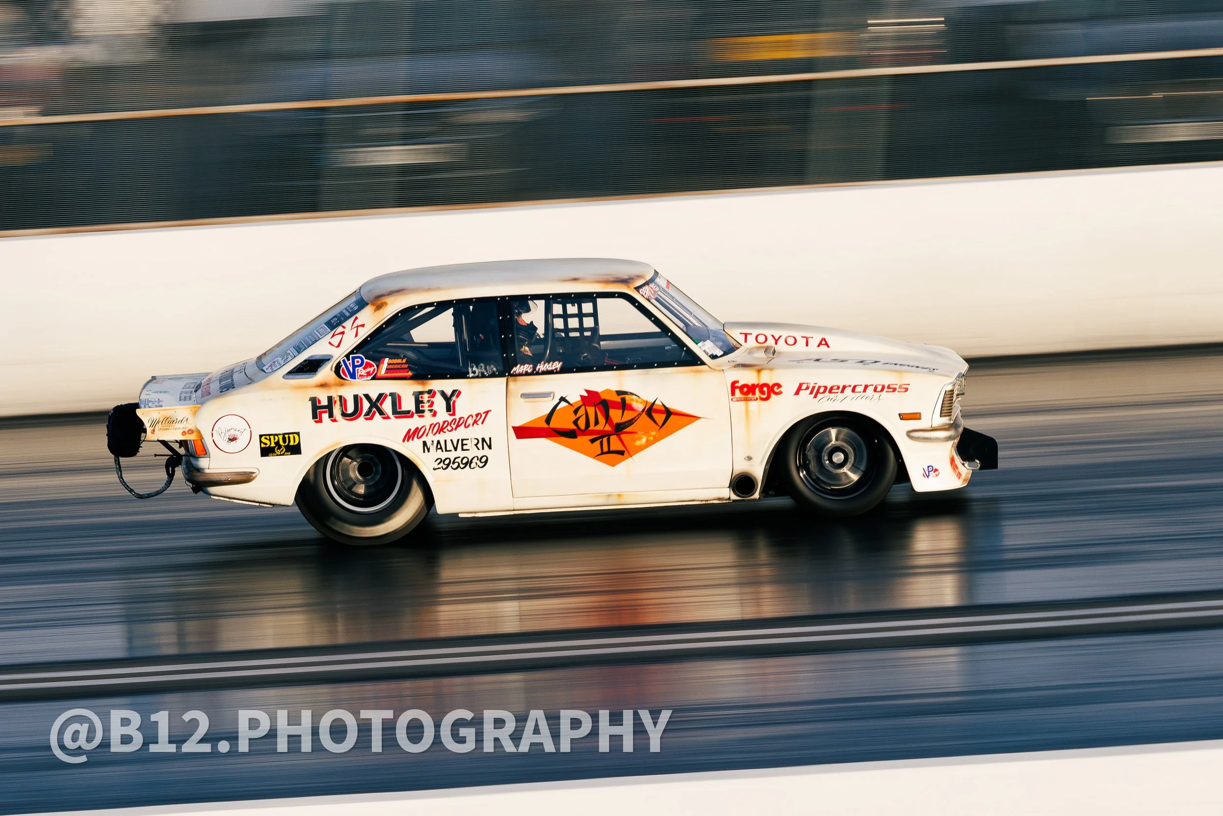 A white vintage race car with various sponsor logos and decals, racing on a track, captured with motion blur.