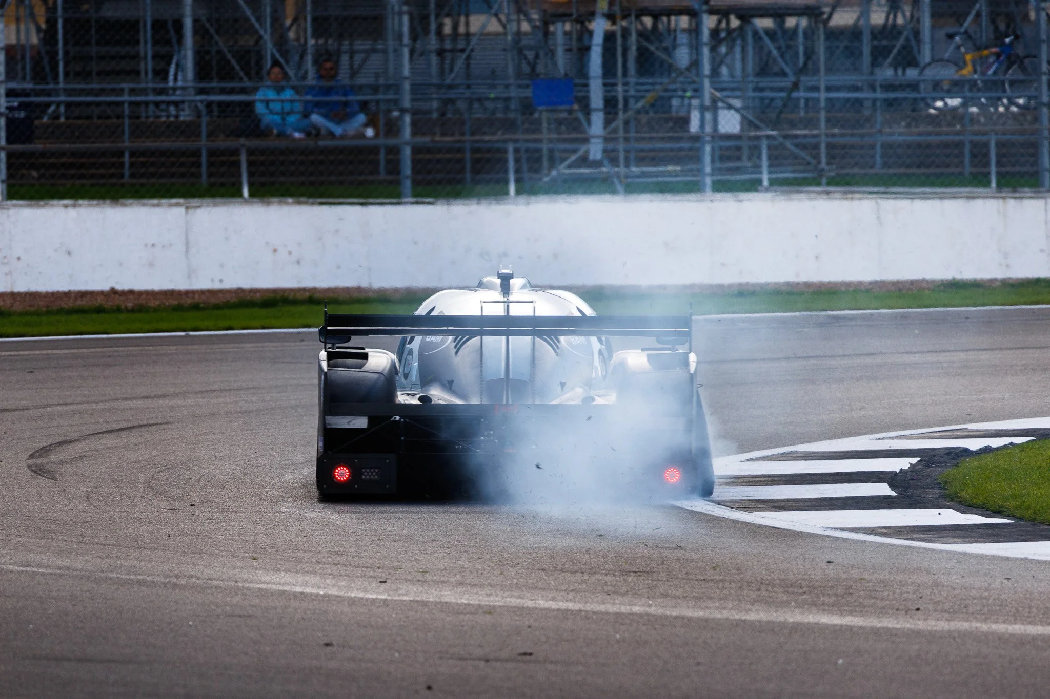 A race car drifting on a race track, creating smoke from the tires with a grandstand and spectators in the background.