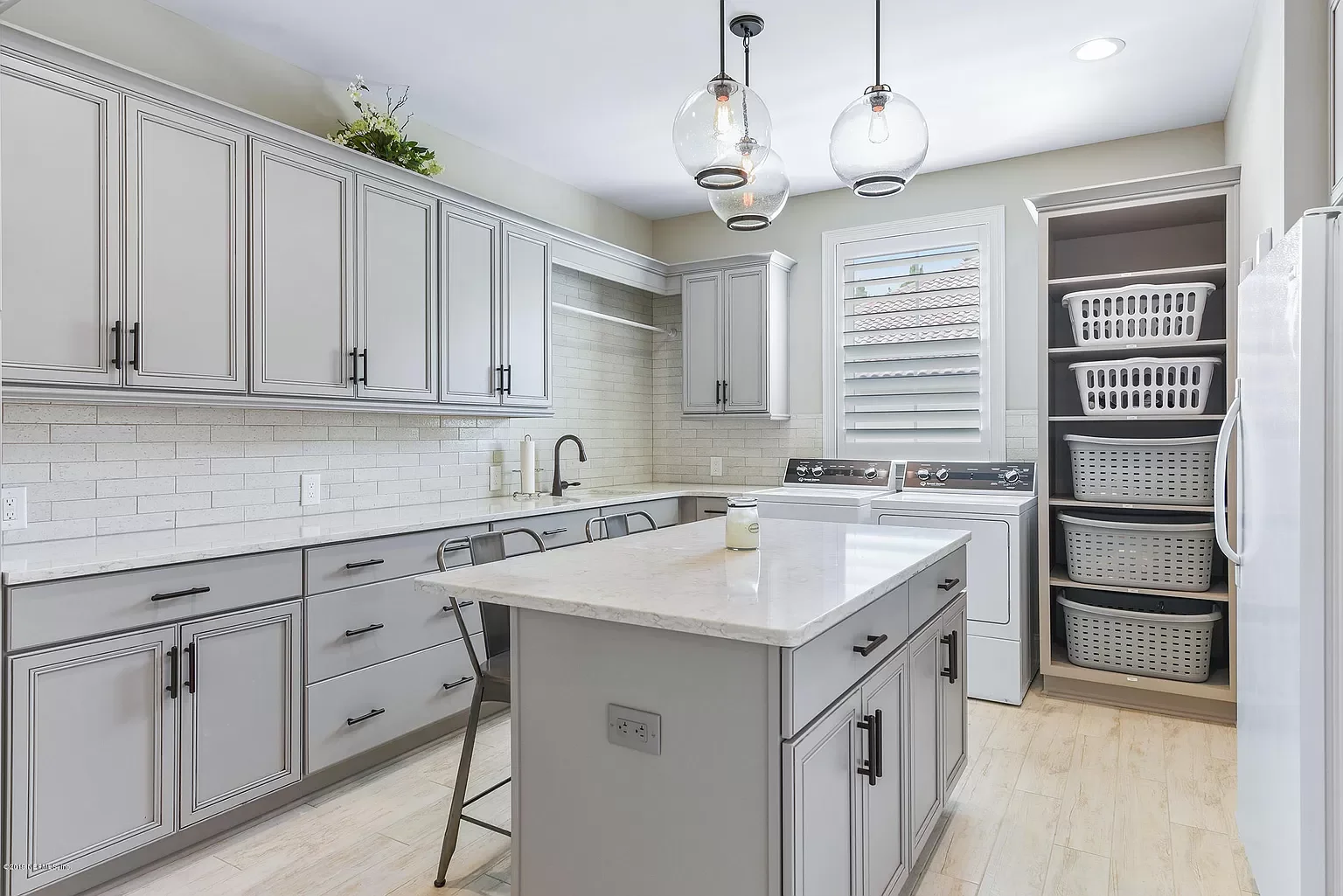 Modern laundry room with white cabinetry, a countertop, washing machine, and shelves with laundry baskets.