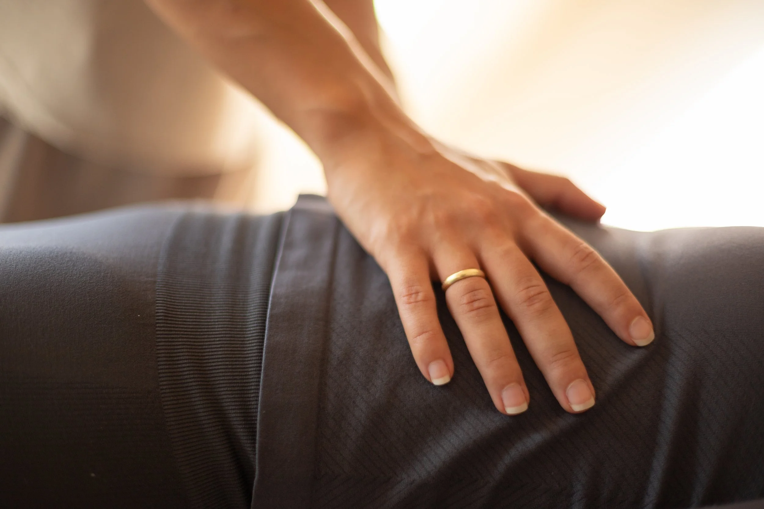Close-up of a person's hand with a wedding ring, resting on the back of another person in a professional suit.