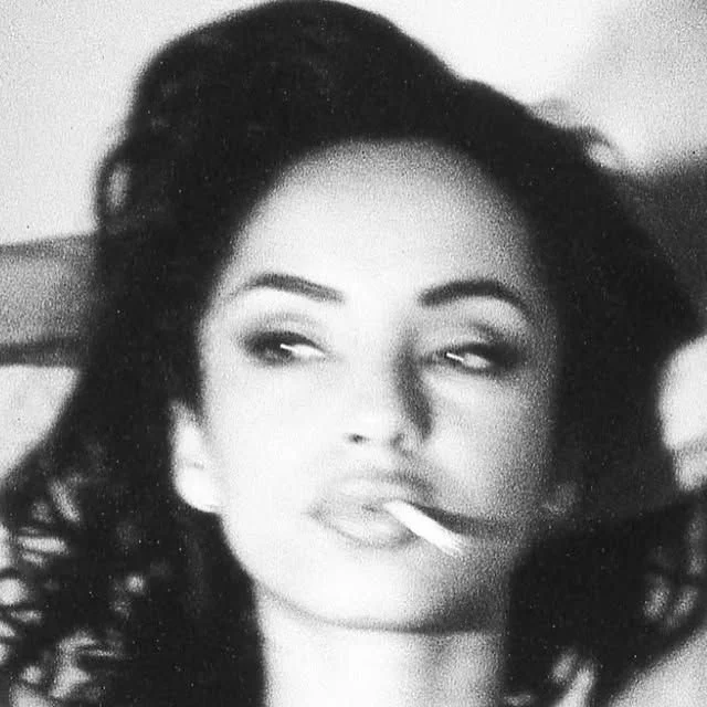 Une jeune femme aux cheveux bouclés, se détendant avec un regard nonchalant, fumant une cigarette.