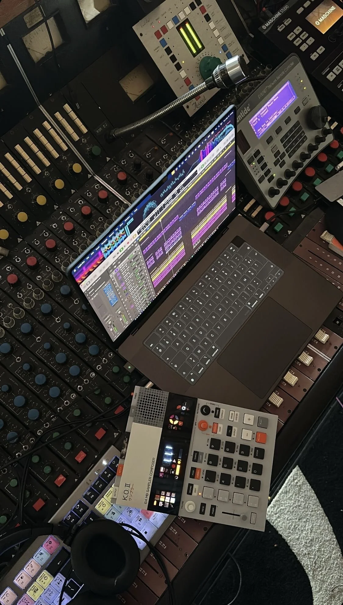 Configuration de matériel de musique électronique avec ordinateur portable affichant un logiciel de production musicale, contrôleurs MIDI, une console de mixage, et d'autres équipements audio.