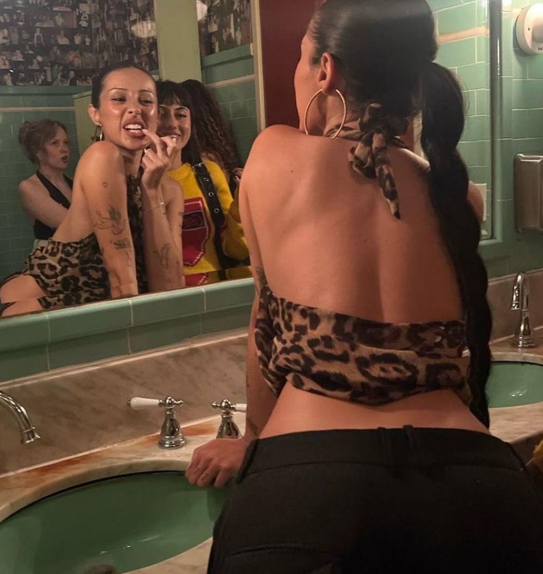 Femme regardant dans un miroir de salle de bain, avec des amis en arrière-plan.