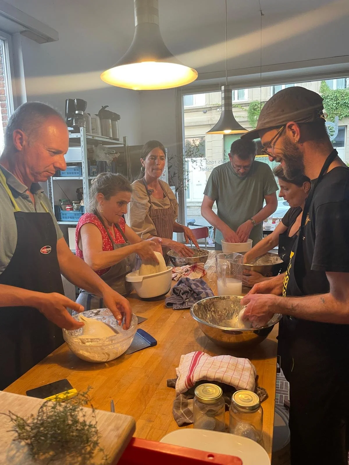 Een groep mensen die in een keuken samen koken en bakken, met verschillende ingrediënten en keukengerei op de tafel.