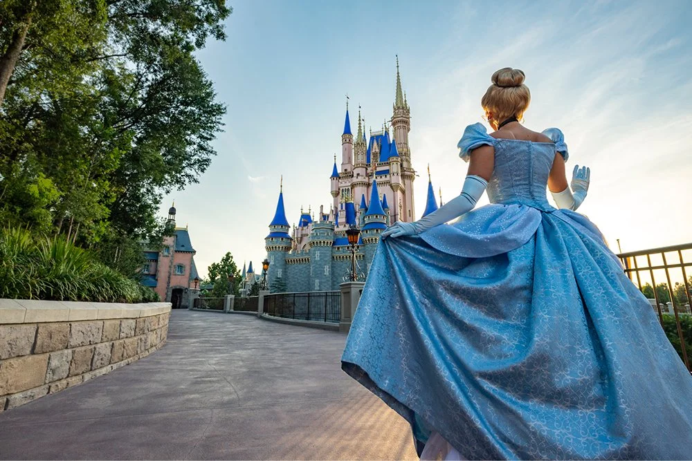 Disney princess in a blue ball gown standing in front of Sleeping Beauty's Castle at Disneyland.