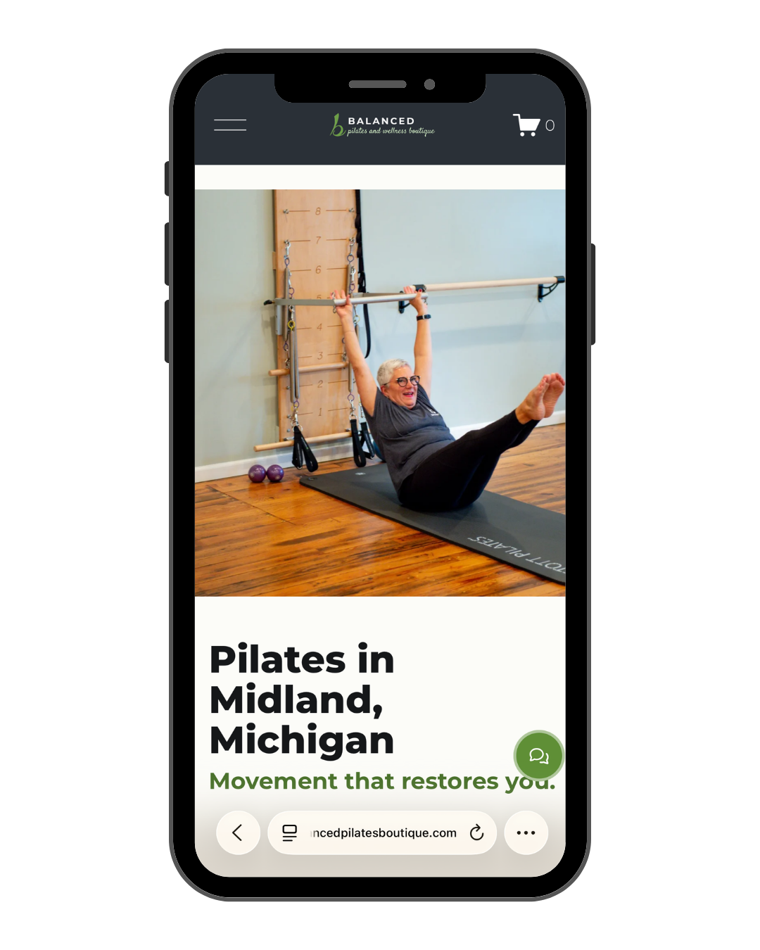 A woman practicing Pilates on a mat in a fitness studio, raising her arms holding a barbell while smiling, with exercise equipment and a wall-mounted ladder in the background.