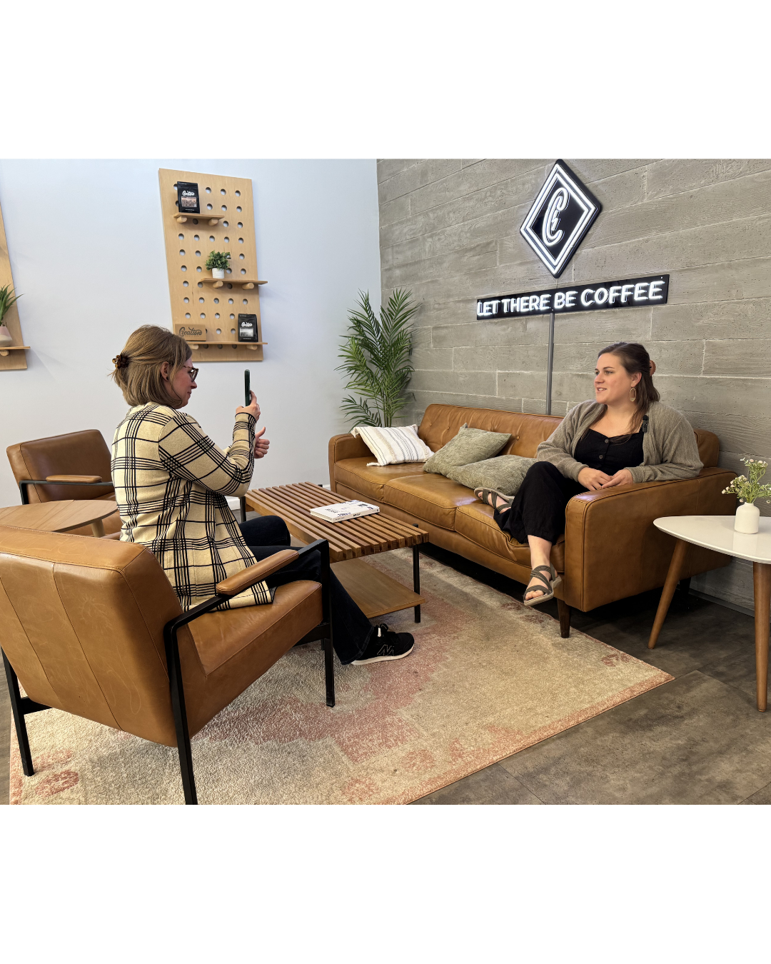 A human-centered content session for a small business in Midland, MI. A business owner smiles while sitting on a tan leather sofa. A creative partner captures story-driven video on a phone in a warm, grounded coffee shop.