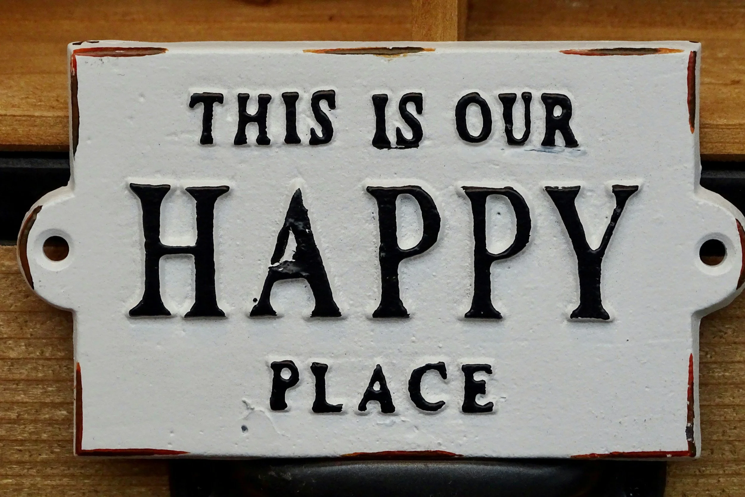 Decorative sign with the text 'This is our happy place' in black letters on a white background, mounted on a wooden surface.