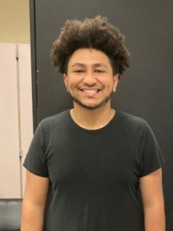 Smiling young man with curly hair wearing a dark t-shirt standing indoors