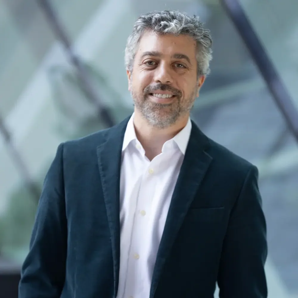 Peter Karol of Abreu Karol Trademark Law with gray hair and a beard wearing a dark blazer and white shirt, smiling at the camera indoors.