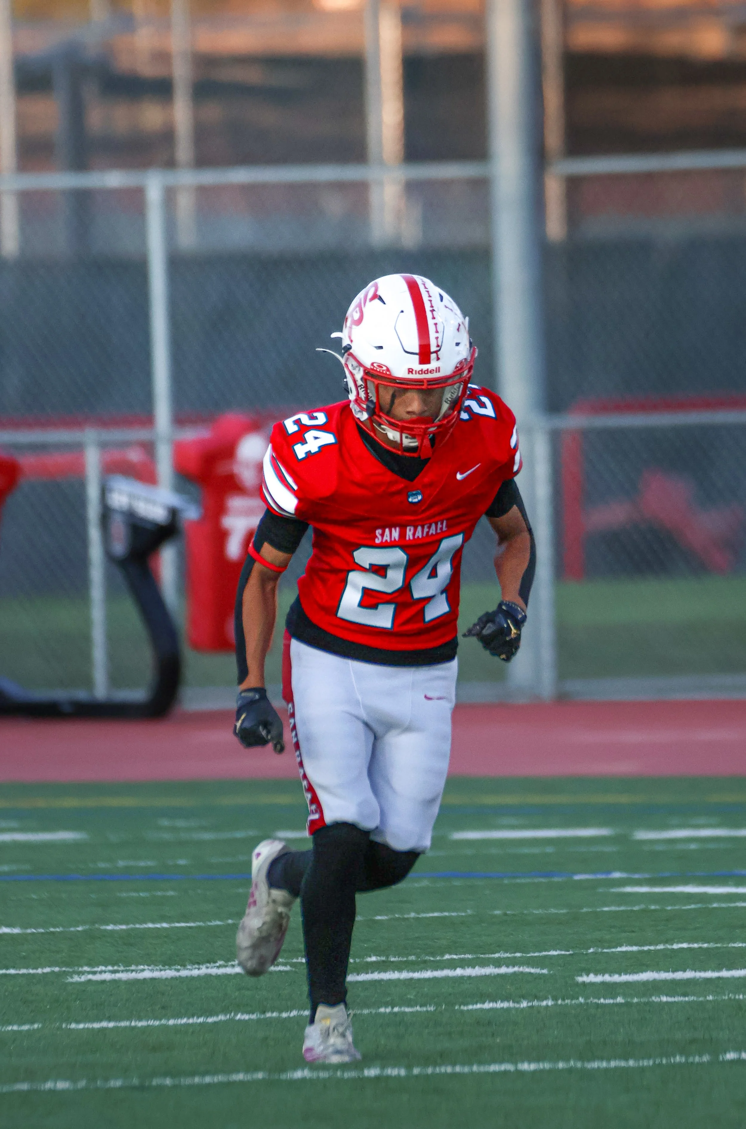An American football player wearing a red jersey with the number 24, white pants, black leggings, a white helmet with red accents, and black gloves, running on a football field during a game.