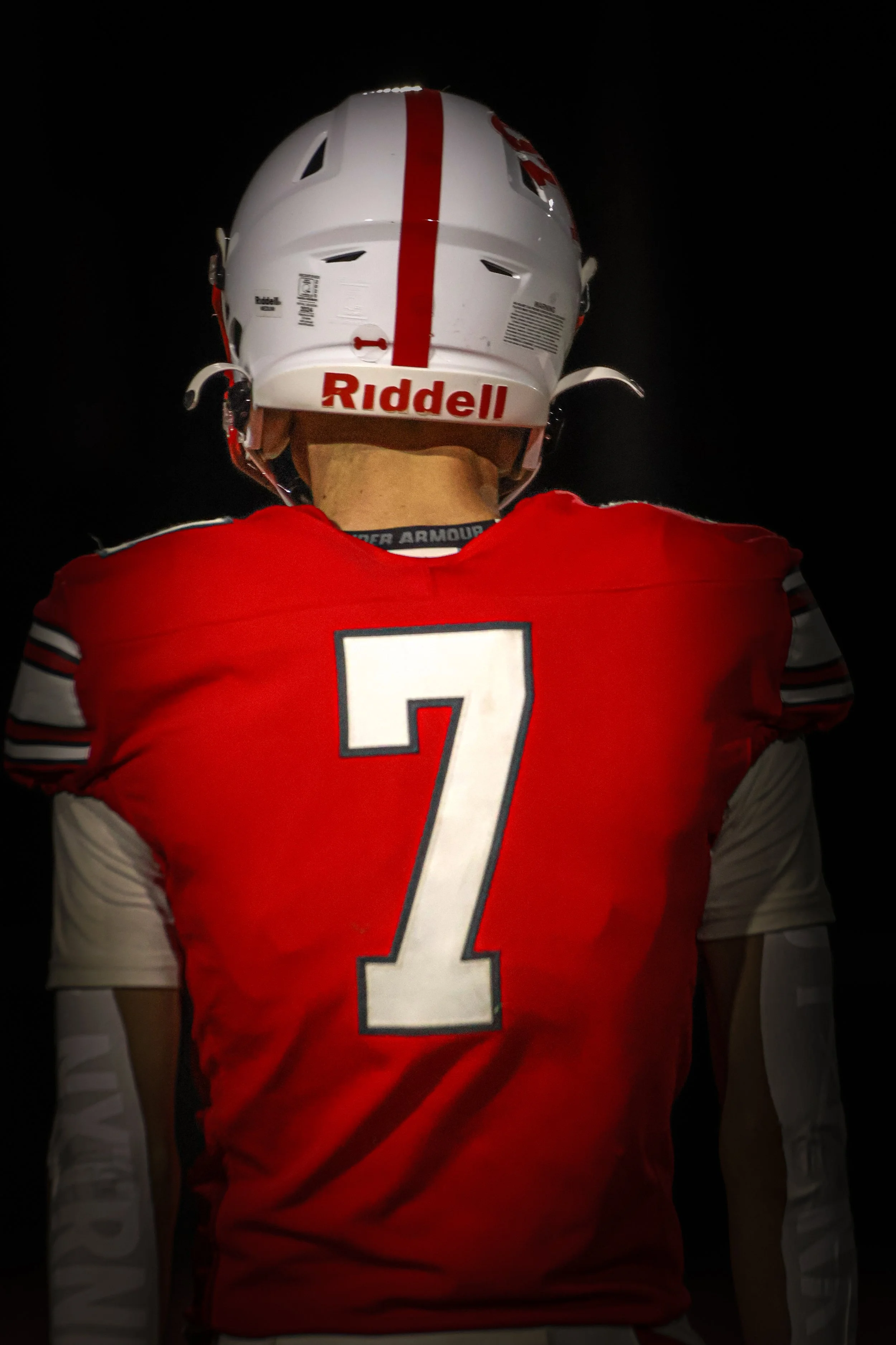 Back of a football player wearing a red and white jersey with the number 7, a white helmet with red stripes and logo, and white sleeves with black stripes.