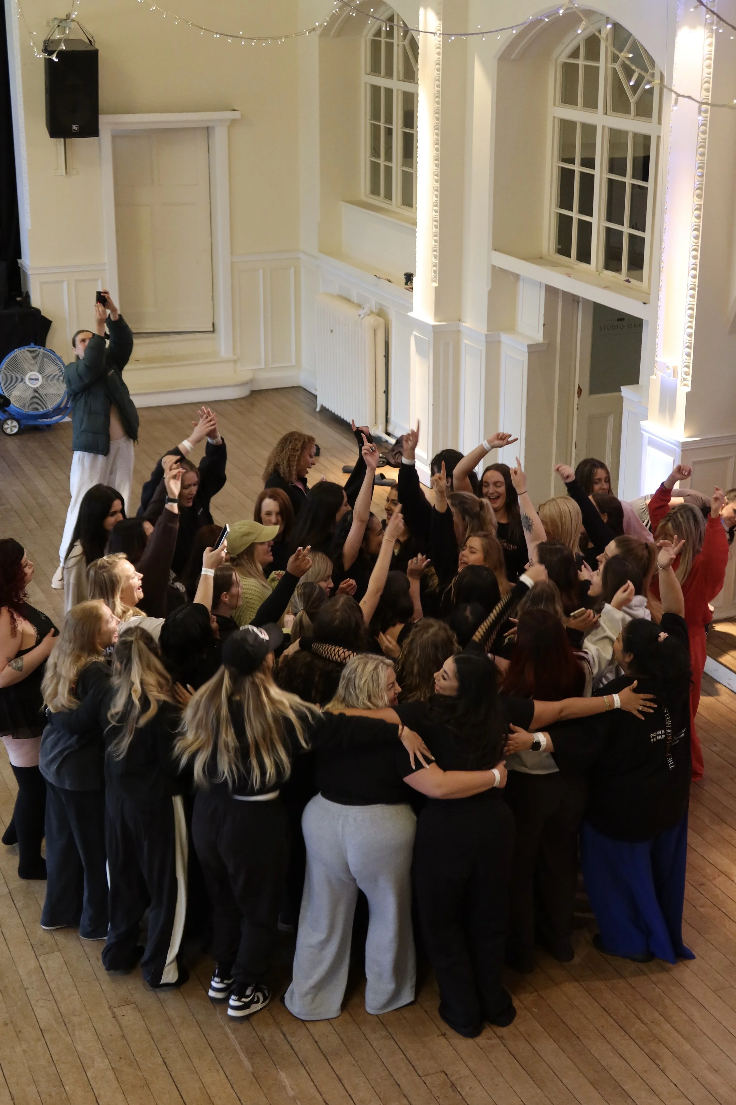 Group of people hugging and celebrating indoors, with some raising their hands and others taking photos.