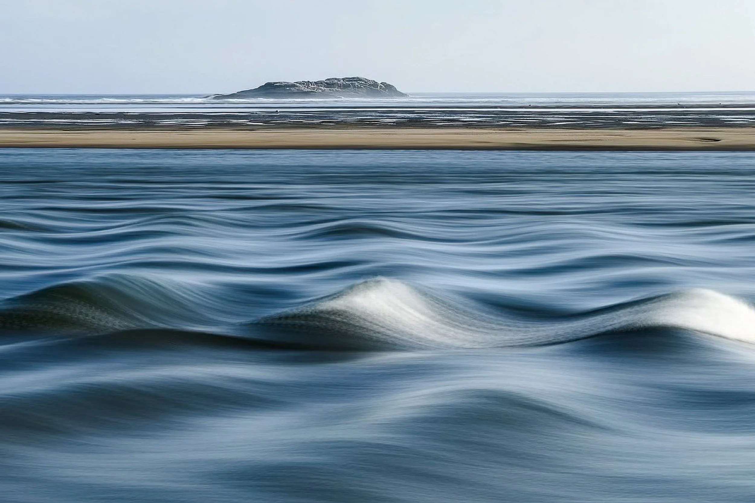 Blue ocean water blurred by motion, with a low sandbar and distant island on the horizon.