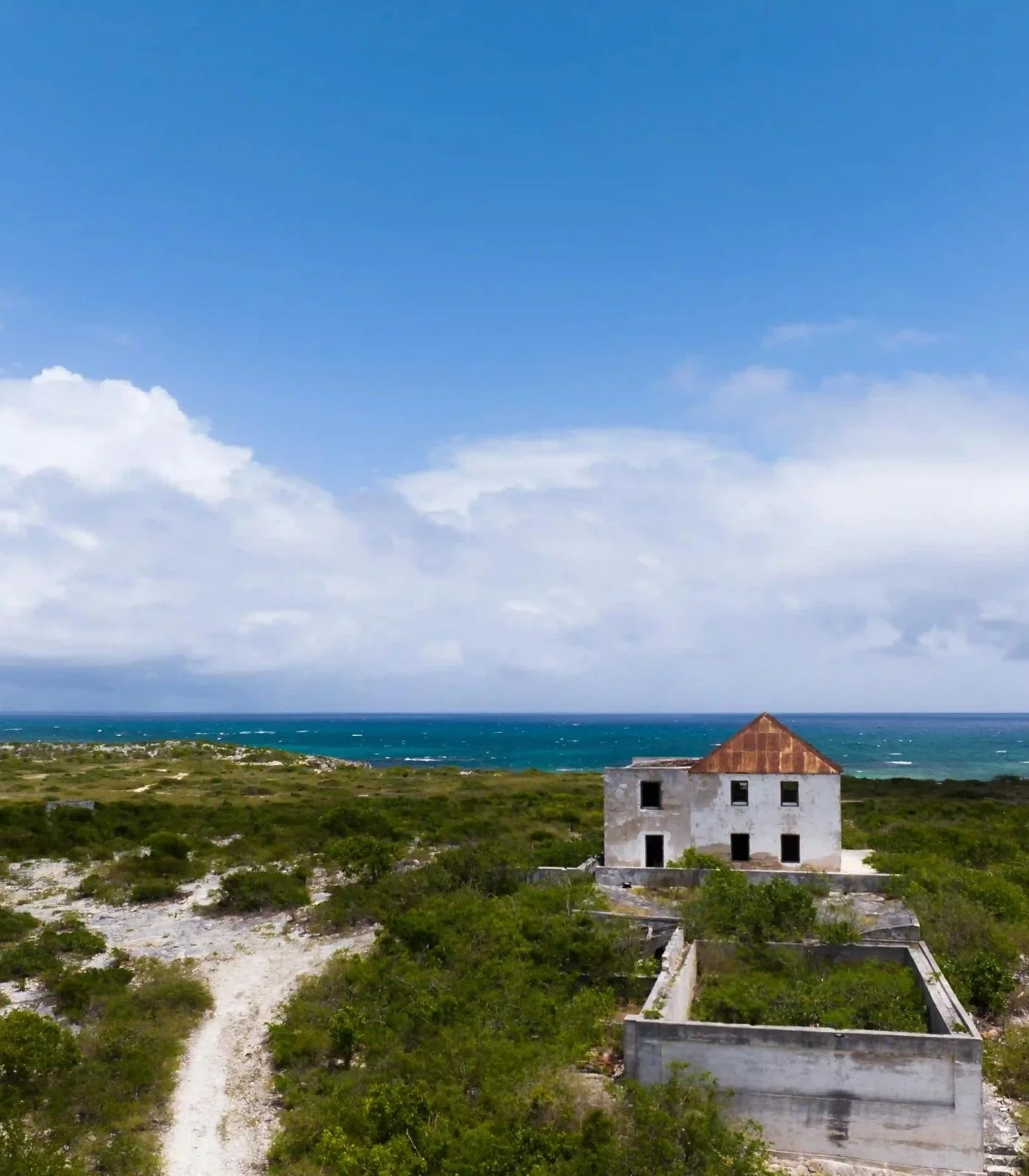 Abandoned house on a grassy landscape with the ocean in the background under a partly cloudy sky.