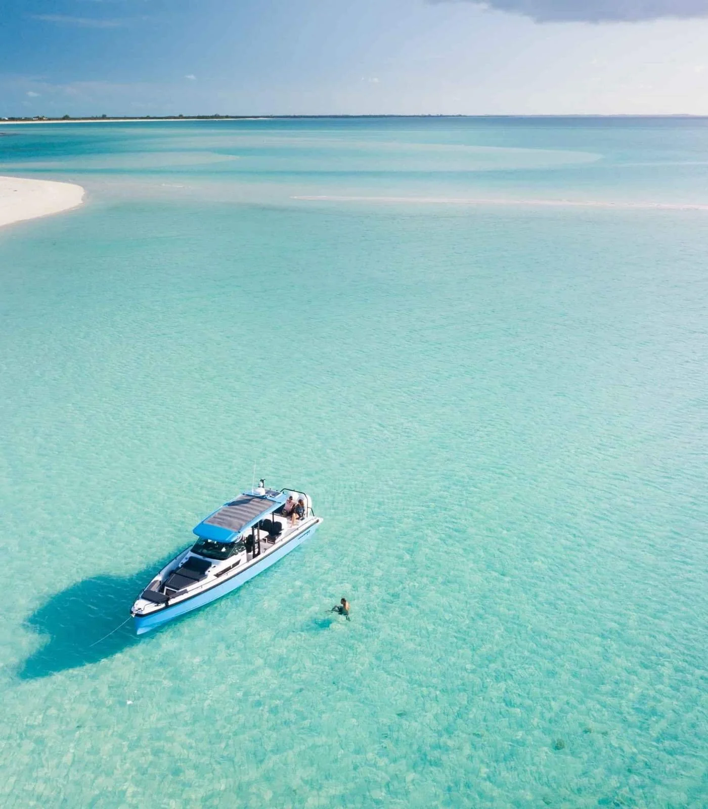 A boat floating on clear turquoise water near a white sandy beach under a blue sky with some clouds.