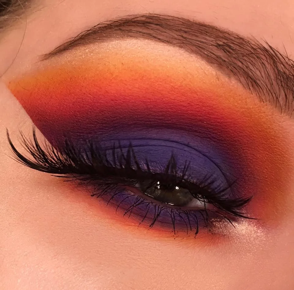 Close-up of an eye with vibrant orange, red, purple eyeshadow blending to create a bold, artistic makeup look.