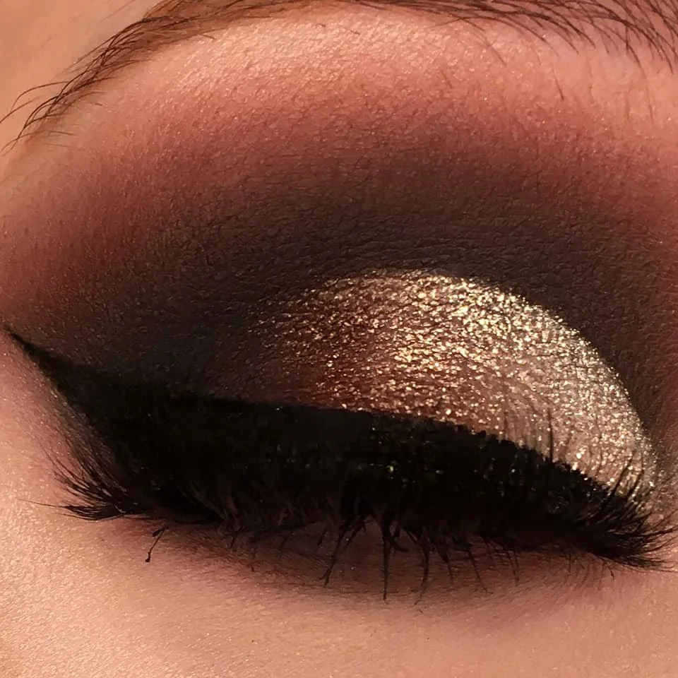 Close-up of a closed eye with shimmery gold and dark eyeshadow, and long eyelashes.