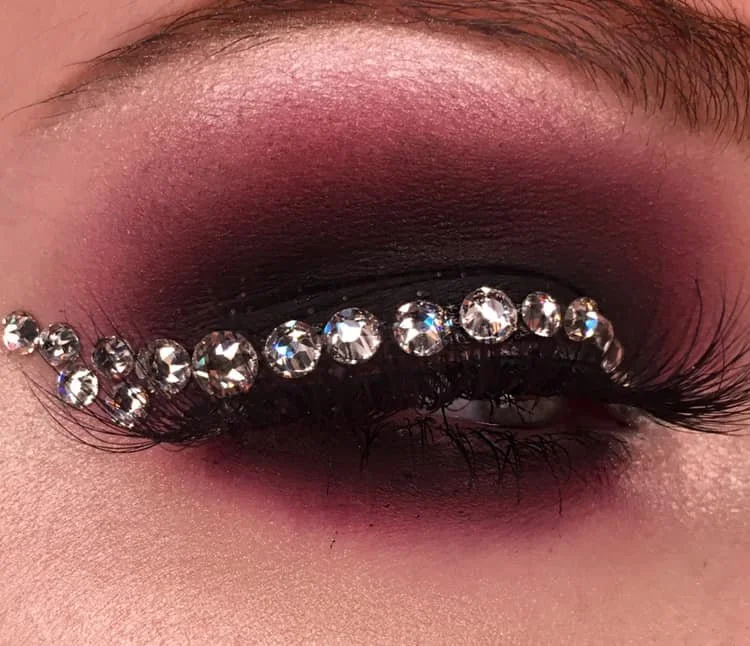 Close-up of a person's eye with dark eyeshadow and rhinestones along the eyelid.