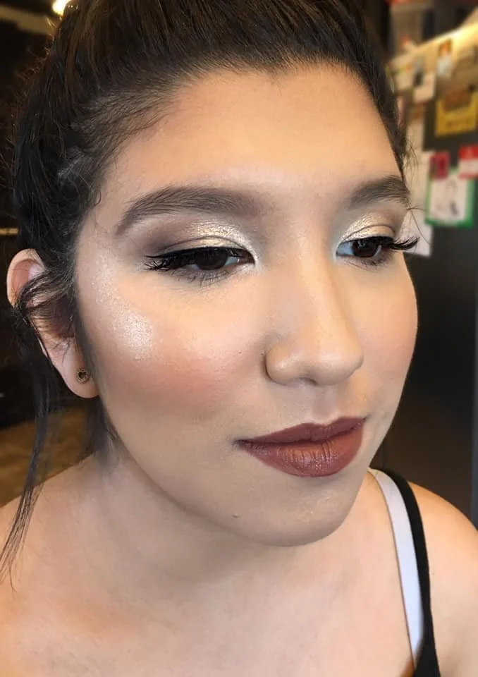 A woman with makeup, including silver eyeshadow, mascara, blush, and brown lipstick, with her eyes mostly closed.