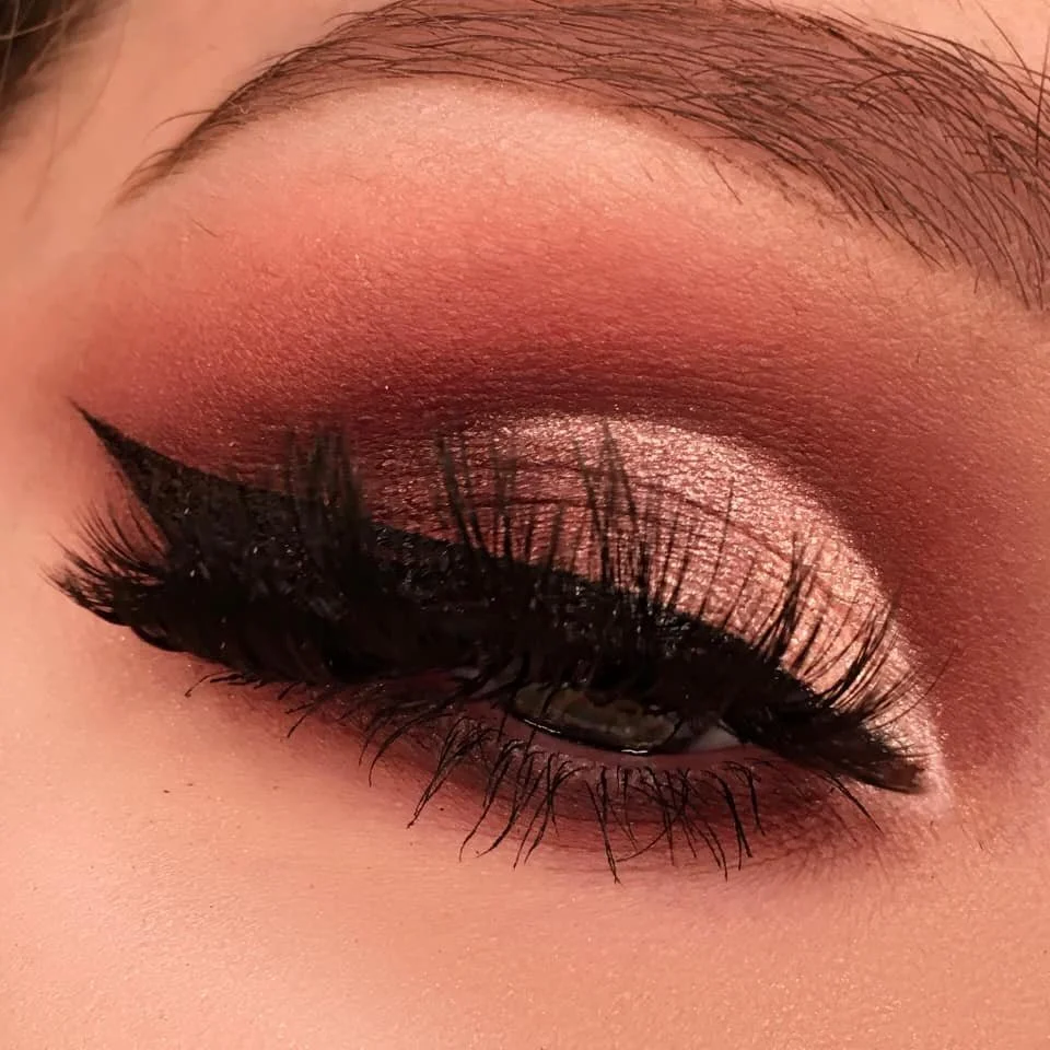 Close-up of a person's eye with pink and brown eyeshadow, dramatic black eyeliner, and long, curled eyelashes.