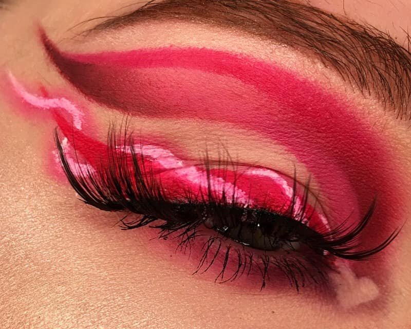 Close-up of eye makeup with pink and red eyeshadow, long false eyelashes, and a matching pink eyeliner wing.