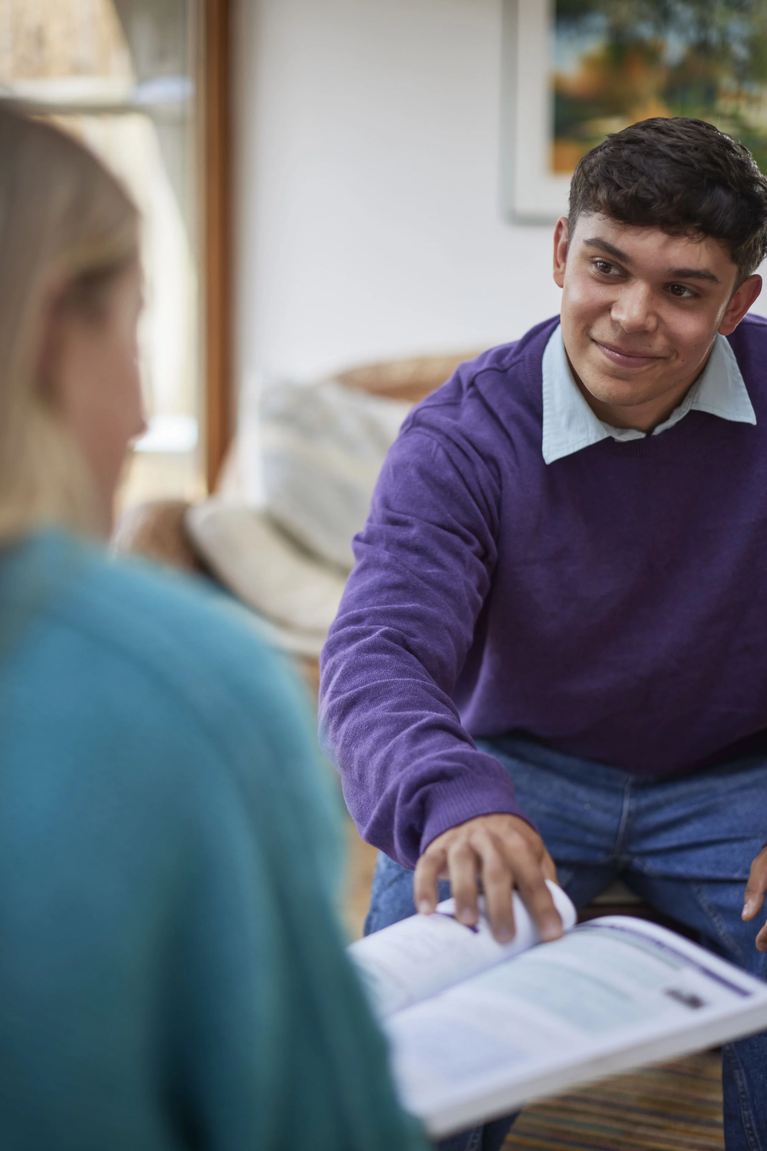 Young man engaging in conversation with woman, holding a book, indoors.